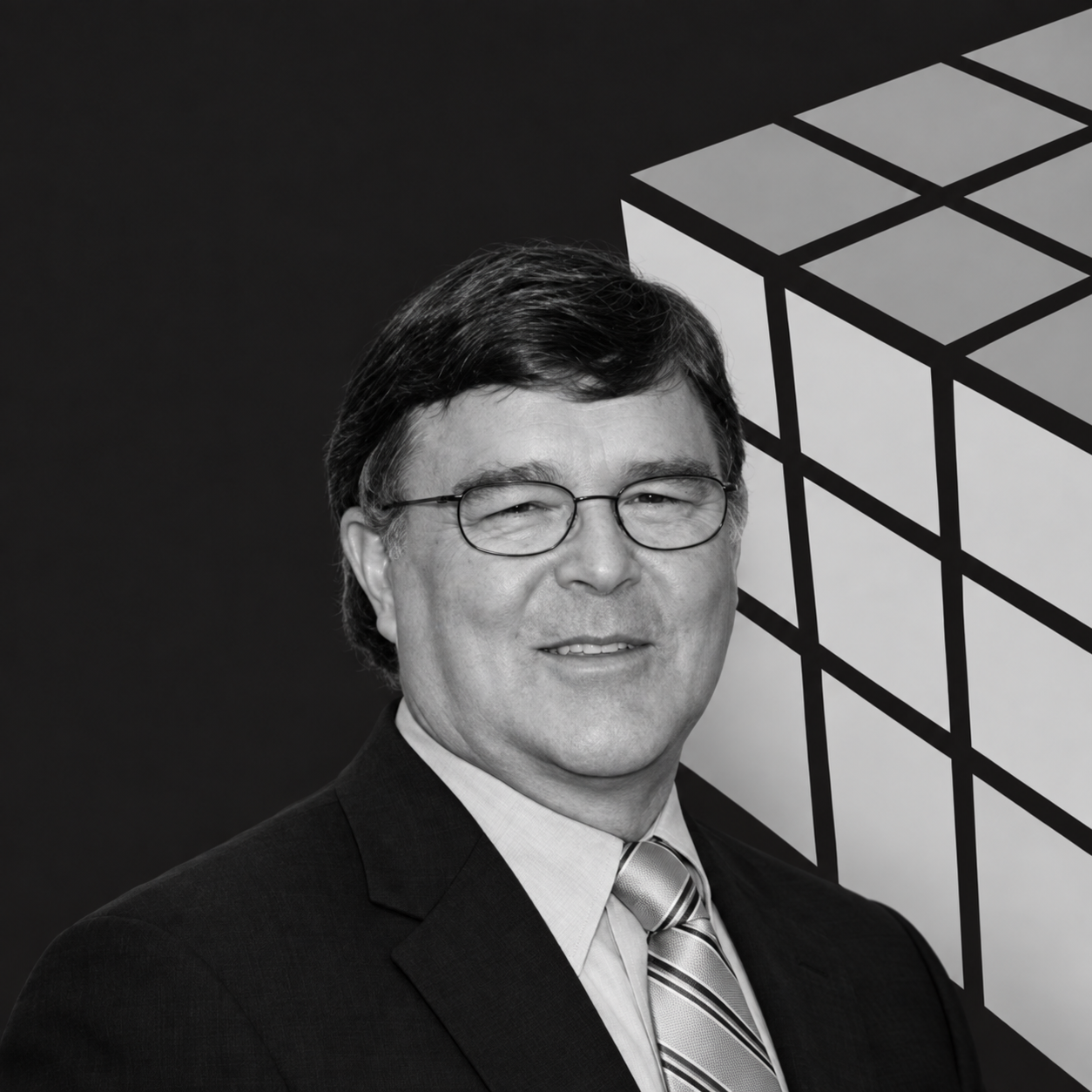 Black and white portrait of a man with glasses, wearing a suit and tie, smiling, with a geometric cube design in the background.