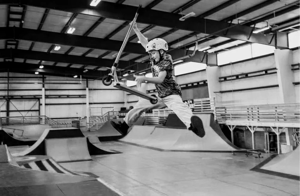 A young child wearing a helmet riding a scooter at an indoor skate park.