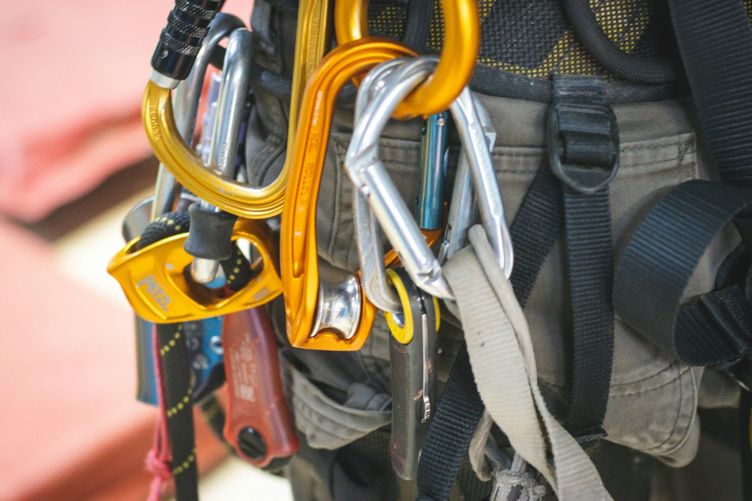 Close-up of climbing gear including carabiners, harness straps, and other equipment attached to a person's waist.