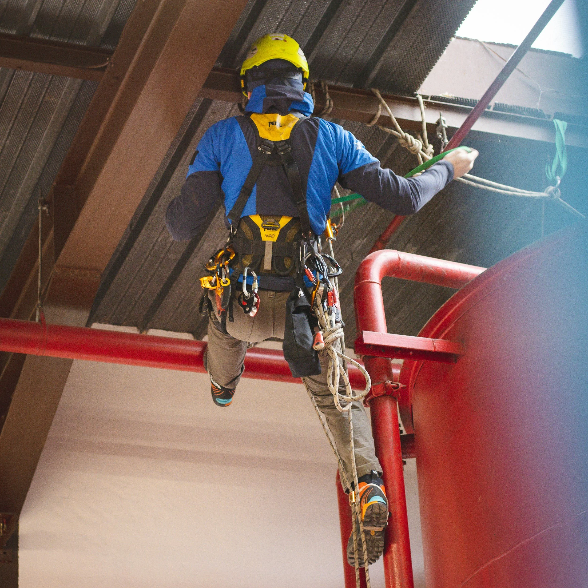 A person slipping or falling while climbing a ladder or scaffolding. The individual is wearing protective gear, including a helmet and harness, and is holding onto ropes or cables.