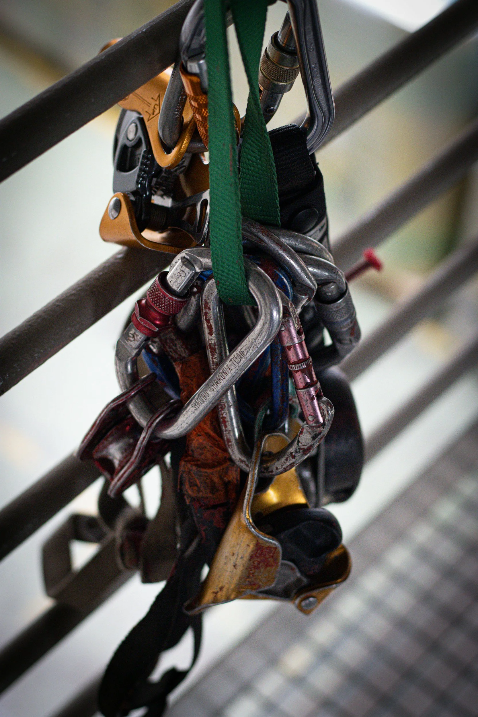 A collection of climbing gear, including carabiners, harnesses, and slings, attached to a metal railing, with the focus on the metal hardware.