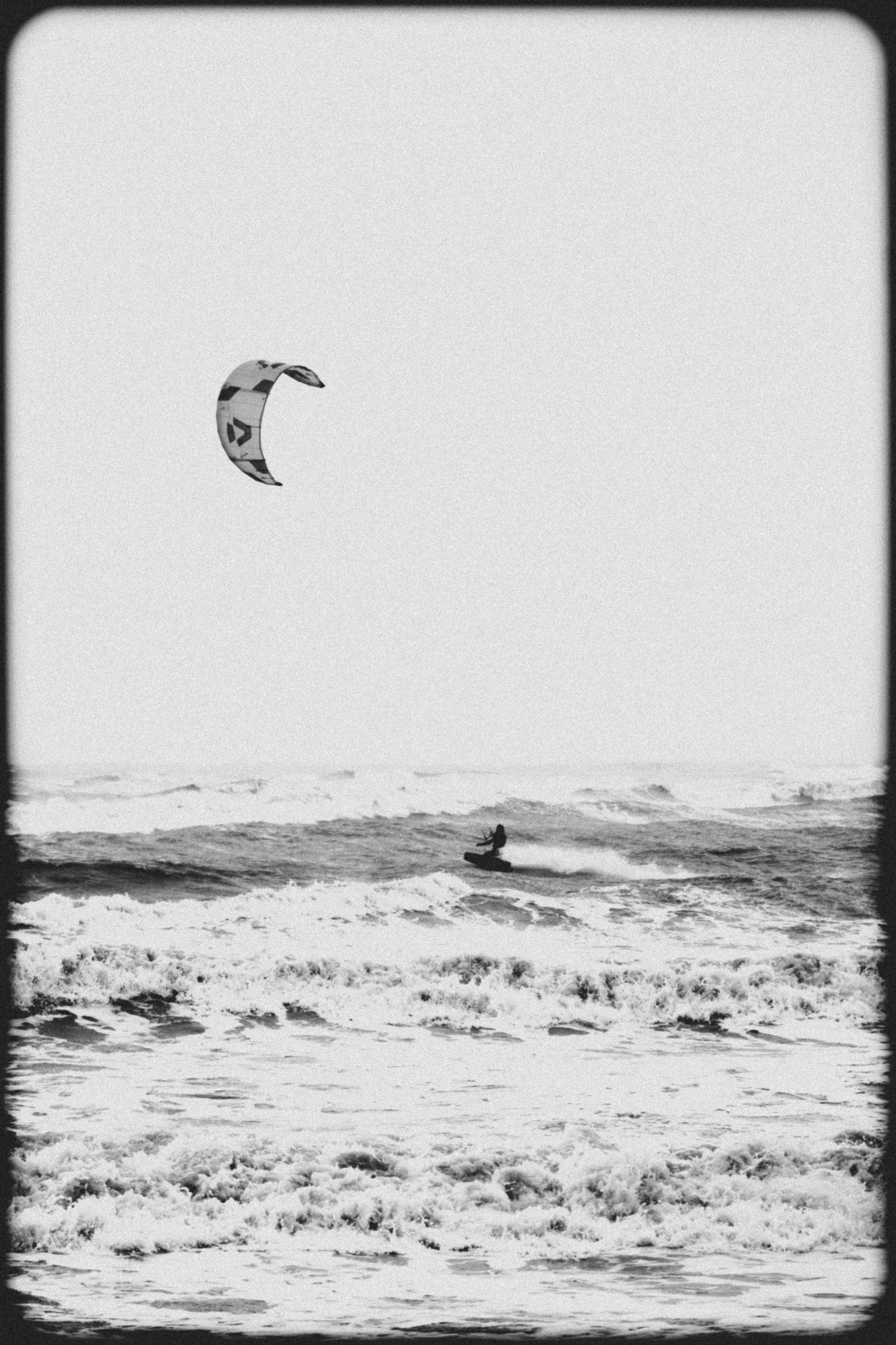 A person kite surfing on the ocean waves, with a kite flying in the sky above.