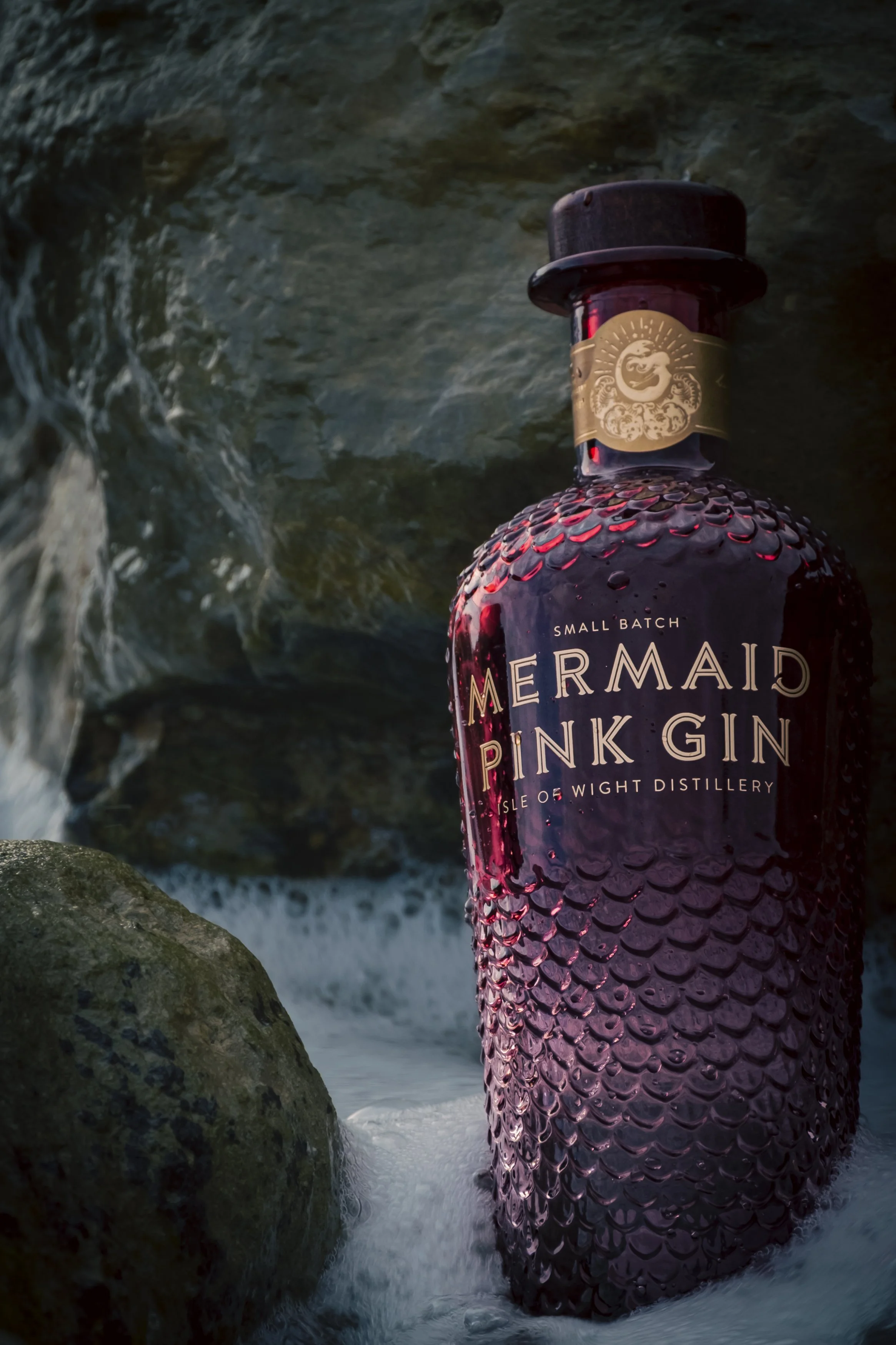 A bottle of Mermaid Pink Gin submerged in water among rocks.