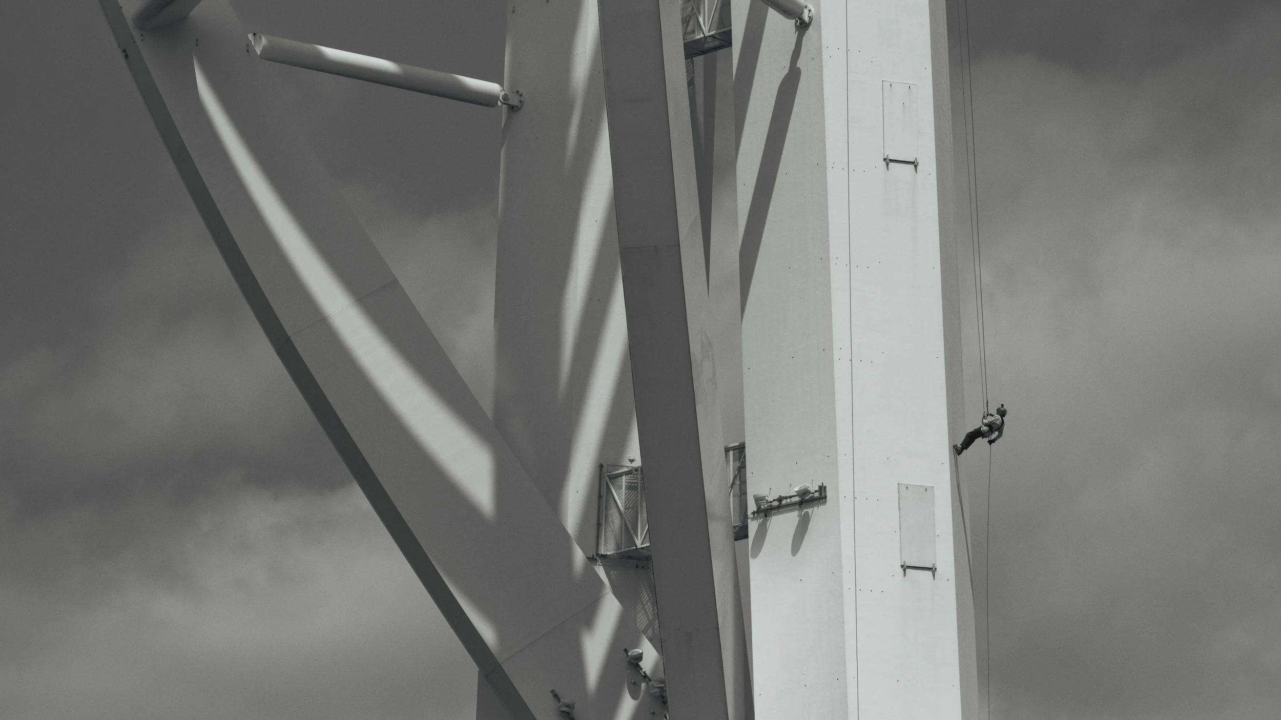A person rappelling down the side of a large, modern building with a white exterior, surrounded by gray clouds in the sky.