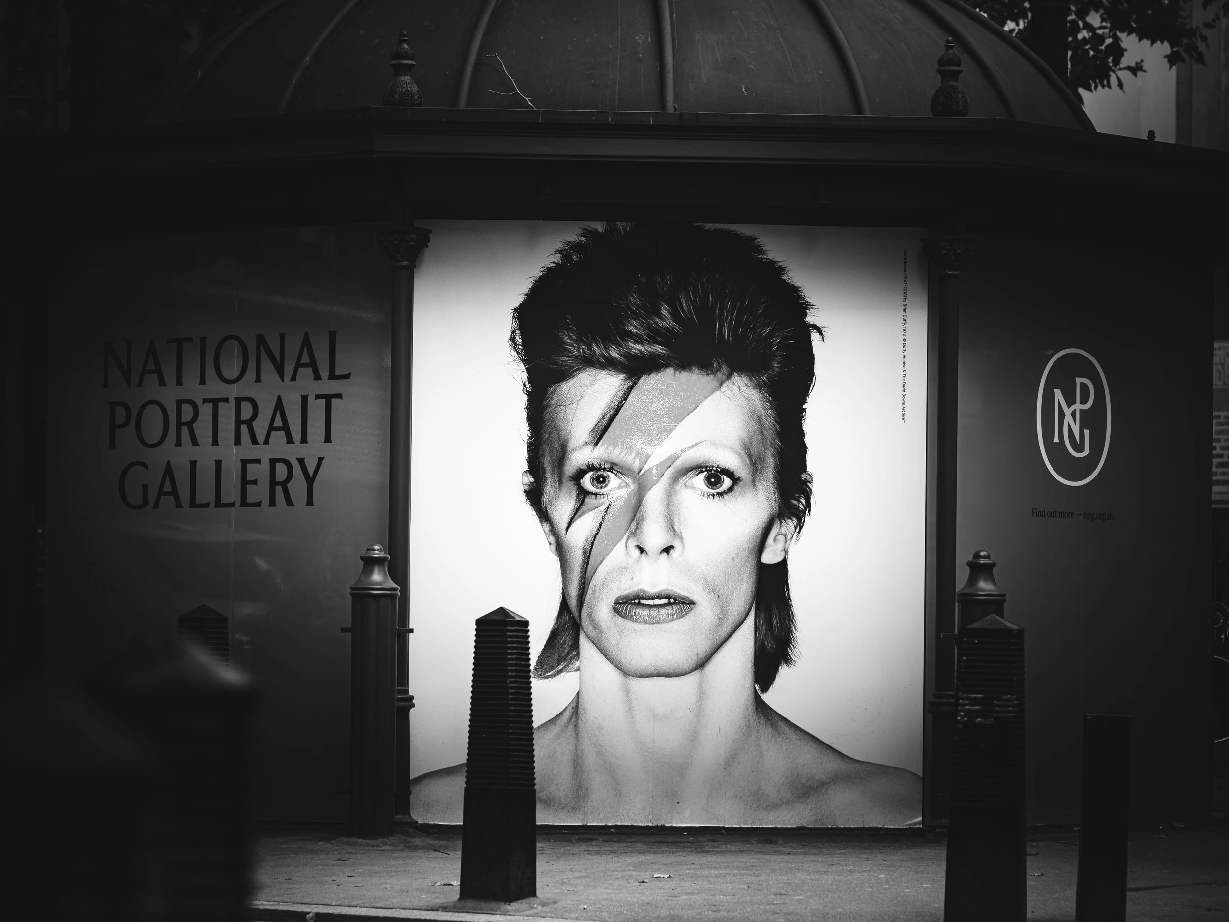 Black and white poster featuring a portrait of David Bowie with a lightning bolt makeup across his face at the National Portrait Gallery.
