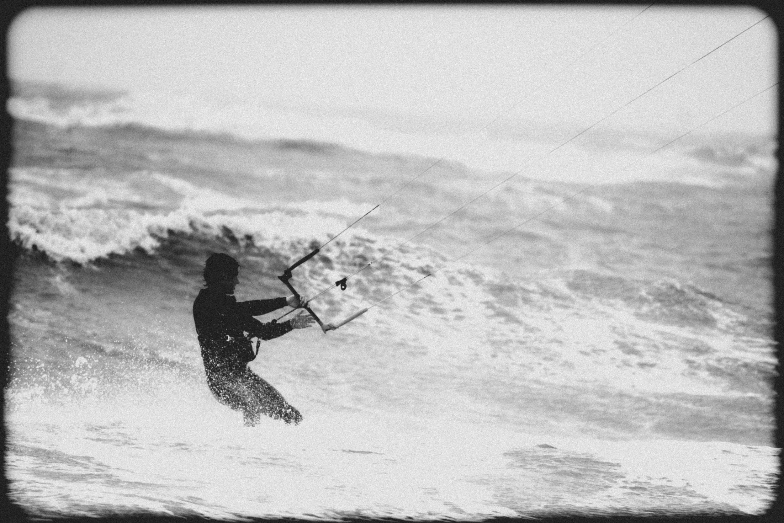 A person kiteboarding on the water with a kite in the sky, surrounded by waves.