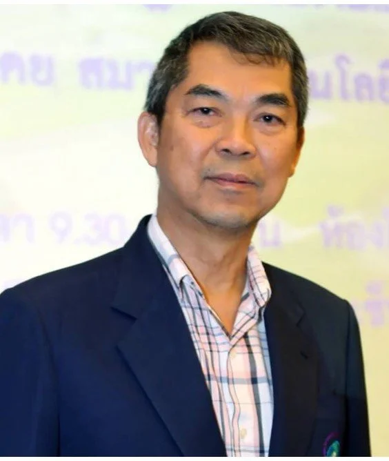 A middle-aged man with short black hair, wearing a dark blazer and a checked shirt, standing in front of a blurred background with purple text.