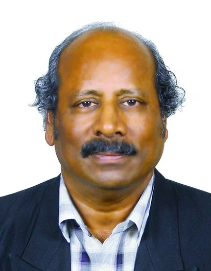 Portrait of a middle-aged man with dark hair, mustache, wearing a dark suit and checkered shirt against a white background.