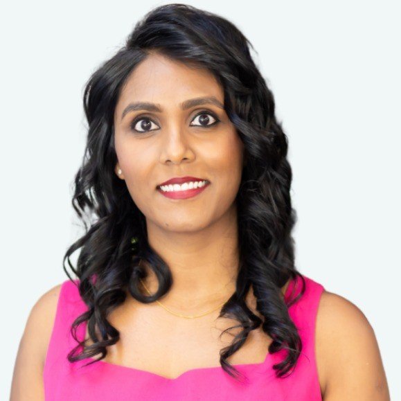 Portrait of a woman with dark curly hair wearing a pink sleeveless top, smiling against a light background.