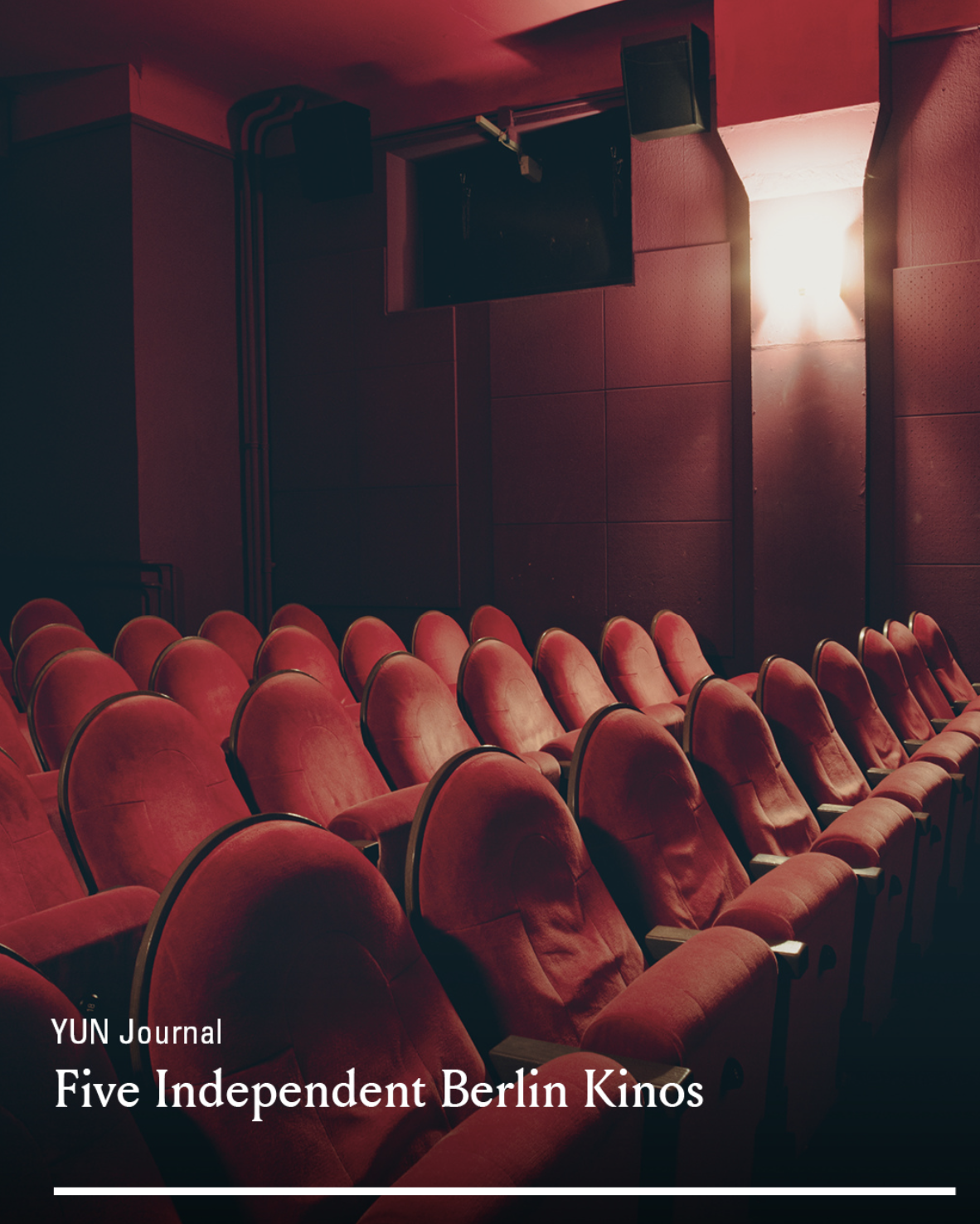 Interior of a movie theater with red cushioned seats and a blank projection screen on the wall, illuminated by soft lighting.