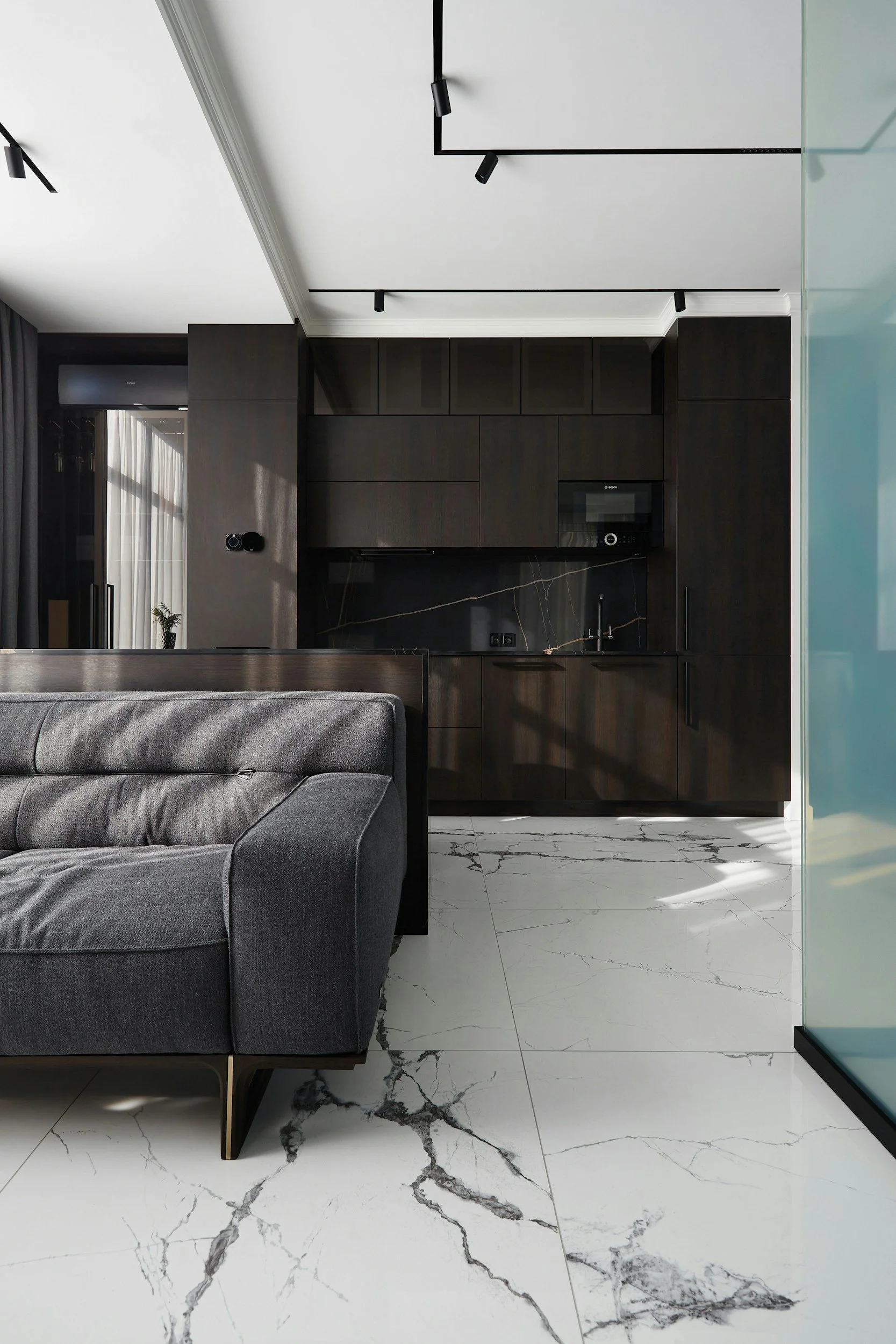 Living room with gray sofa, black cabinets, white marble floor with black veining, and black track lighting on ceiling.