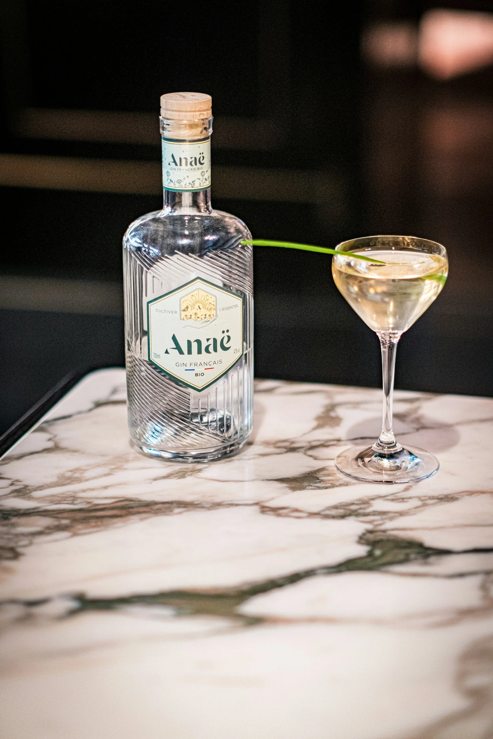 A bottle of Anaé French gin with a glass of gin and tonic on a marble surface.