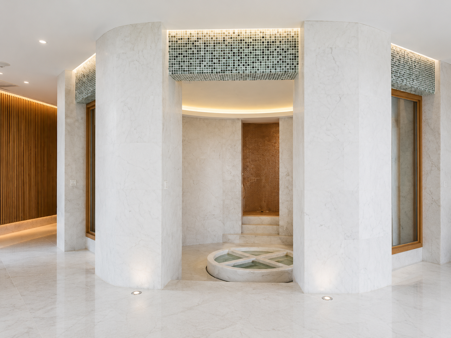 Modern spa with marble walls and floors, featuring a circular fountain, steps leading to a small shower area, and illuminated ceiling details.