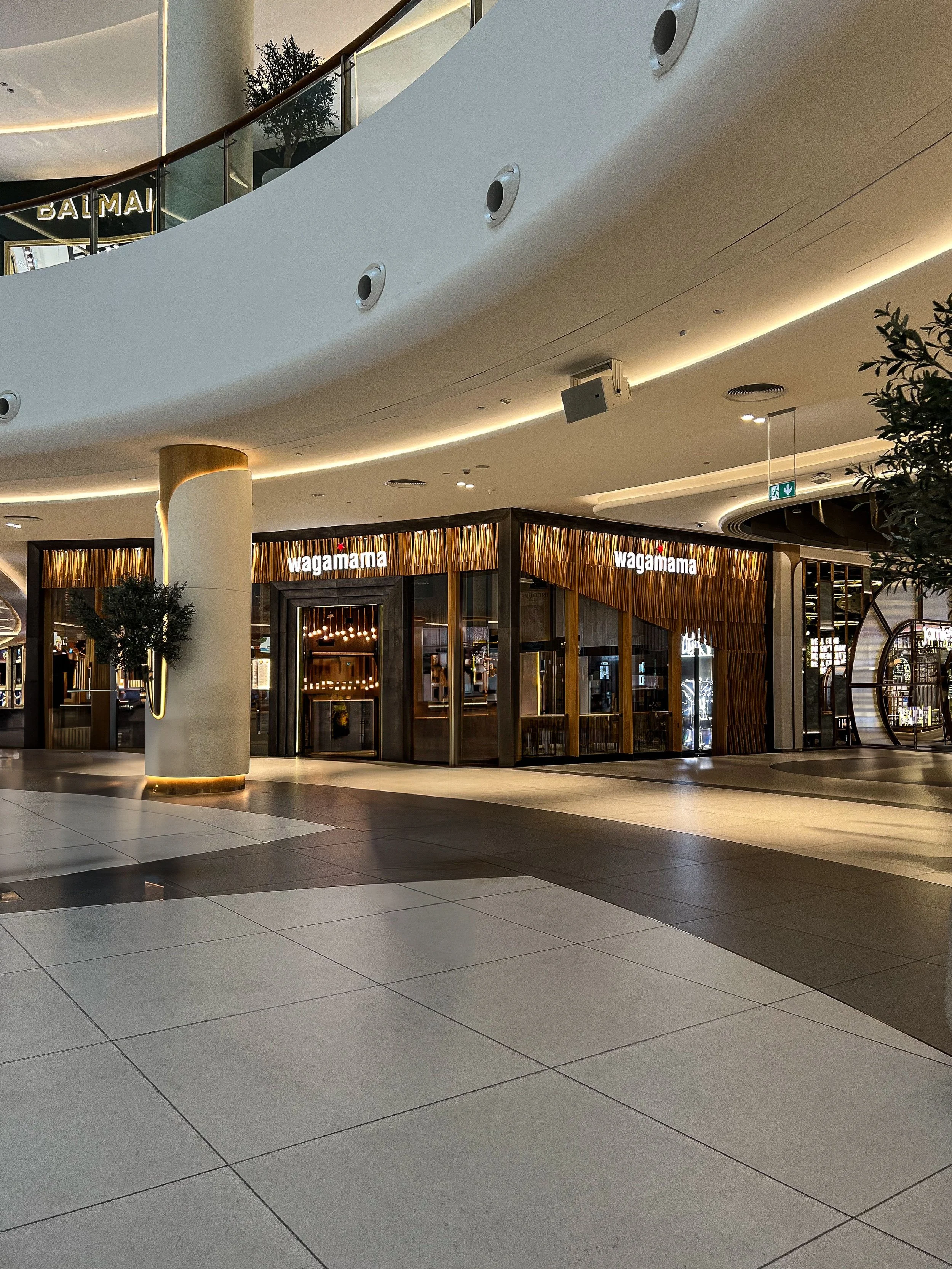 Interior of a shopping mall featuring a Wagamama restaurant, with modern design elements, lighting, and decorative plants.
