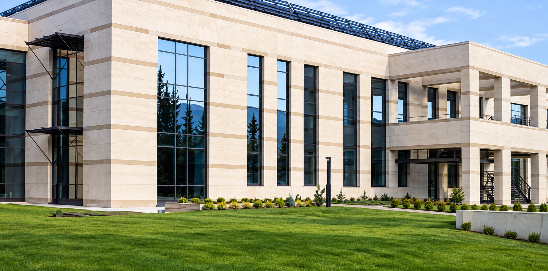 Modern office building with large glass windows, beige stone exterior, and well-maintained green lawn.