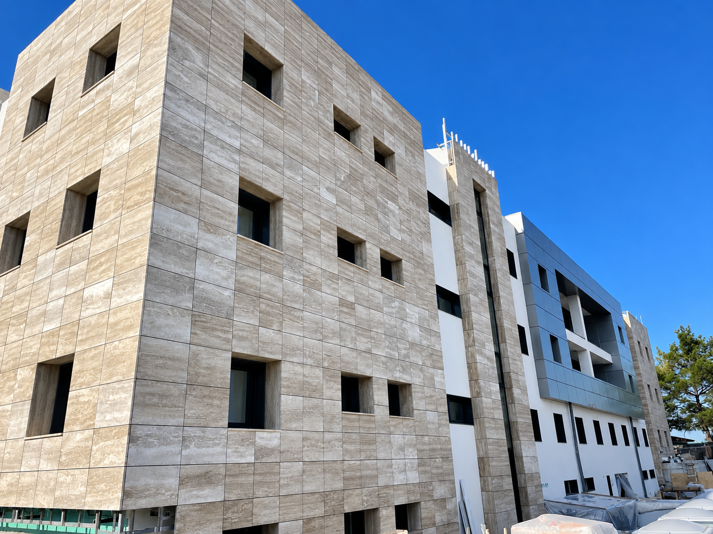 Modern multi-story building with beige stone and white and blue panel accents, under clear blue sky.