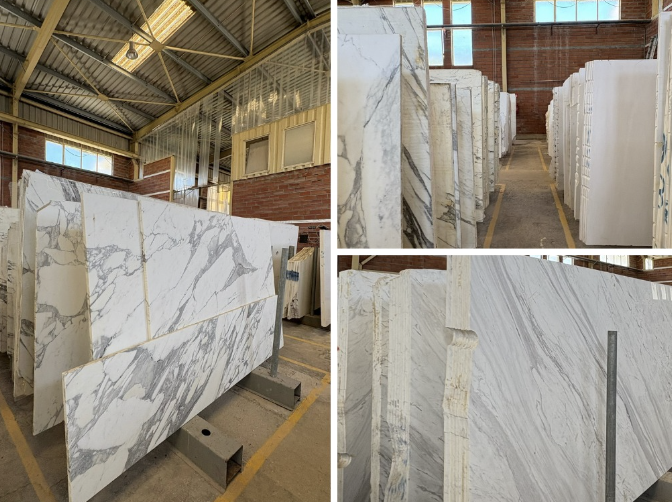 Display of various white and gray marble slabs with natural veining, stored indoors.
