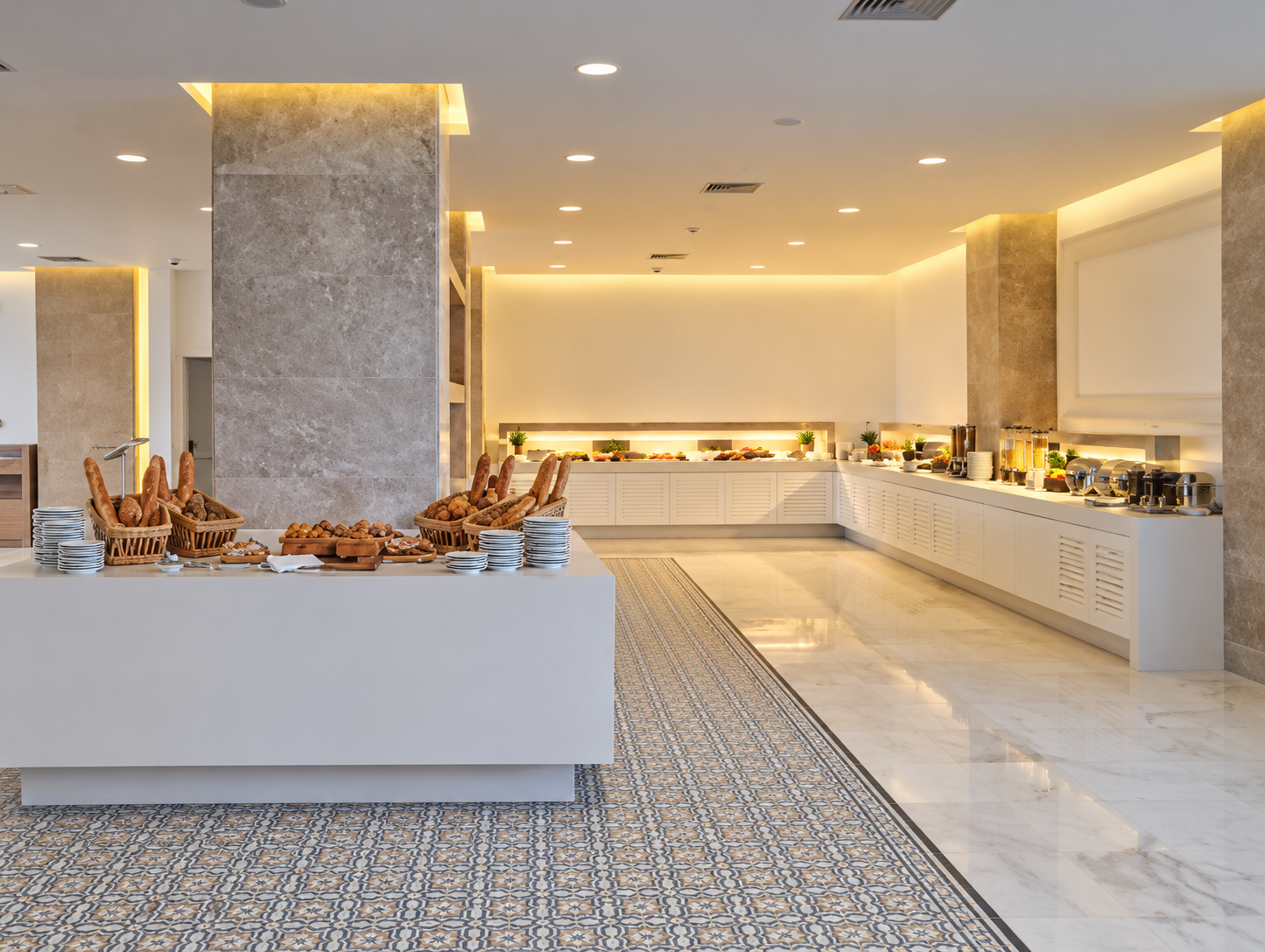 Buffet table with bread and pastries in a bright, modern dining area with a food station in the background.