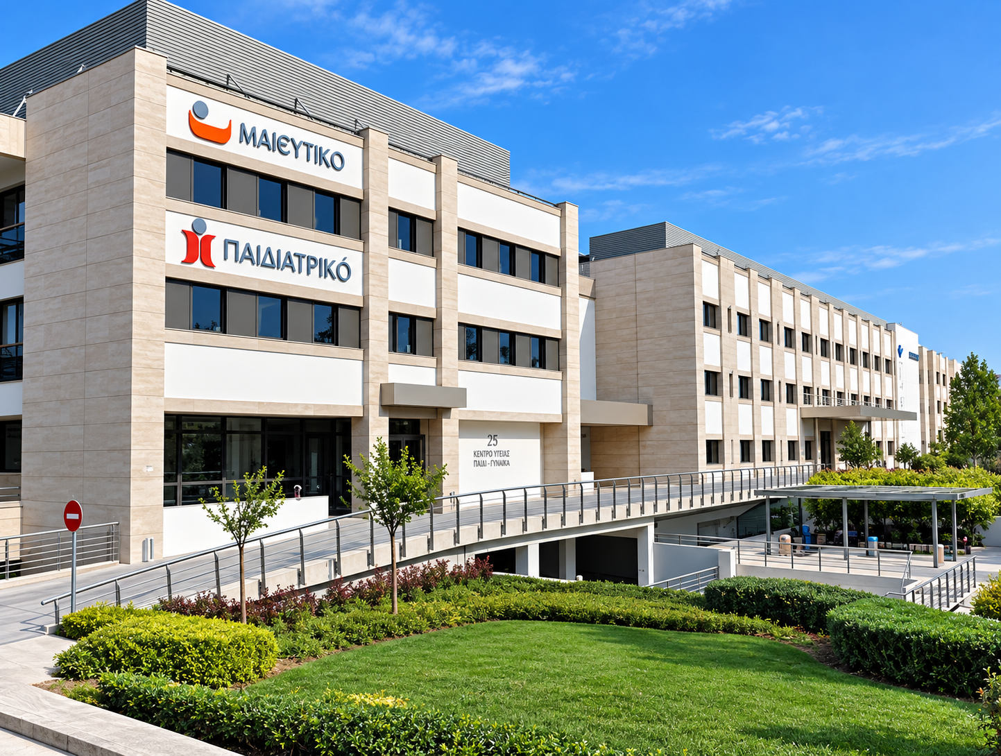 Modern hospital building with Greek signage, surrounded by greenery and a blue sky.