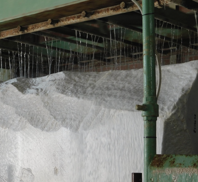 Close-up of a salt production process showing salt crystals forming on a surface beneath a pipe system.