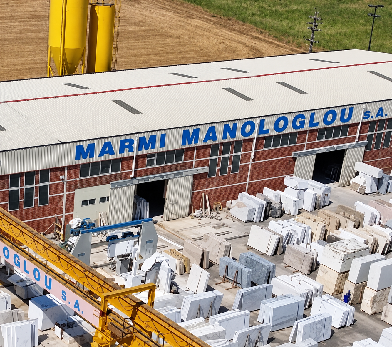 A building labeled 'Marmi Manologlou S.A.' with marble slabs outside and construction equipment nearby.