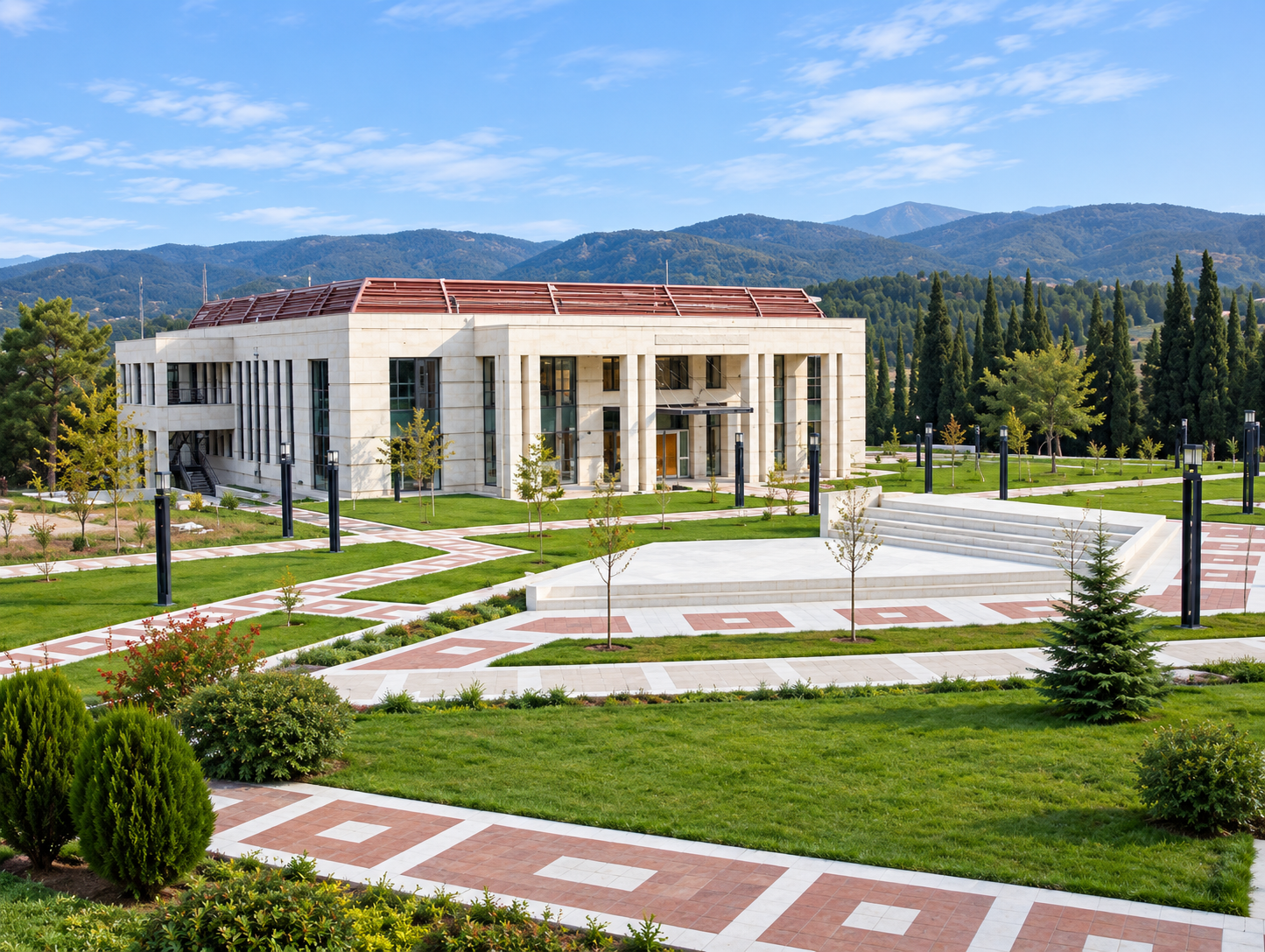 A modern building with a red roof situated in a landscaped area with pathways, small trees, and greenery, backed by mountains and a partly cloudy sky.