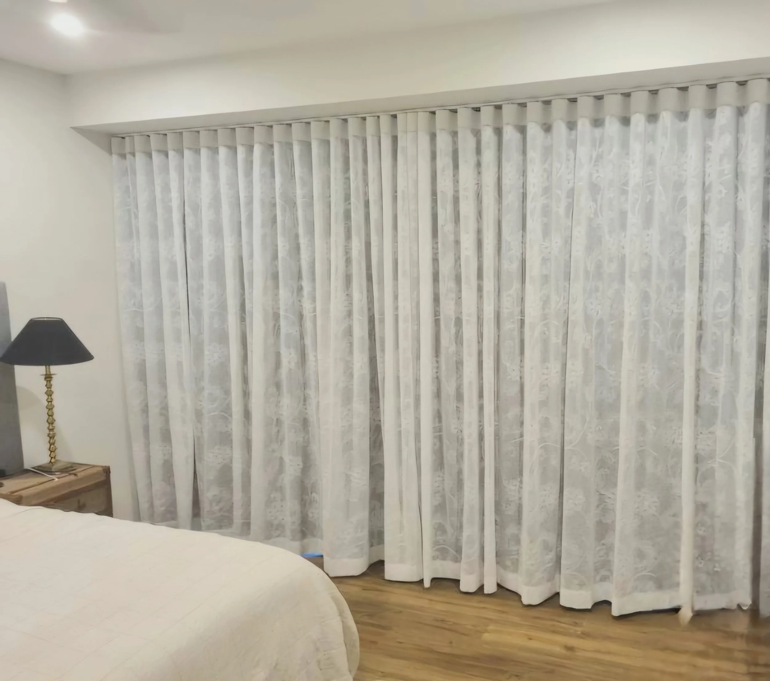 Photo of white marble curtains hanging in a living room with a brass floor lamp on the left side.