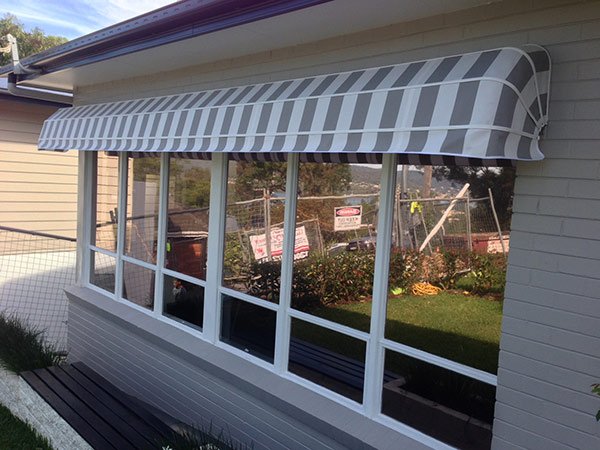 A white house with large windows covered by a striped fabric awning, and a black wooden deck in front of the windows.