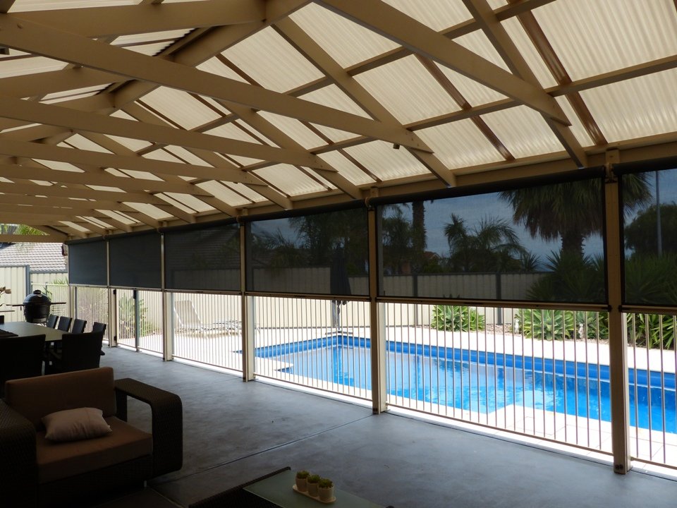 Covered patio area overlooking a backyard swimming pool with a metal fence, outdoor furniture, and palm trees in the background.