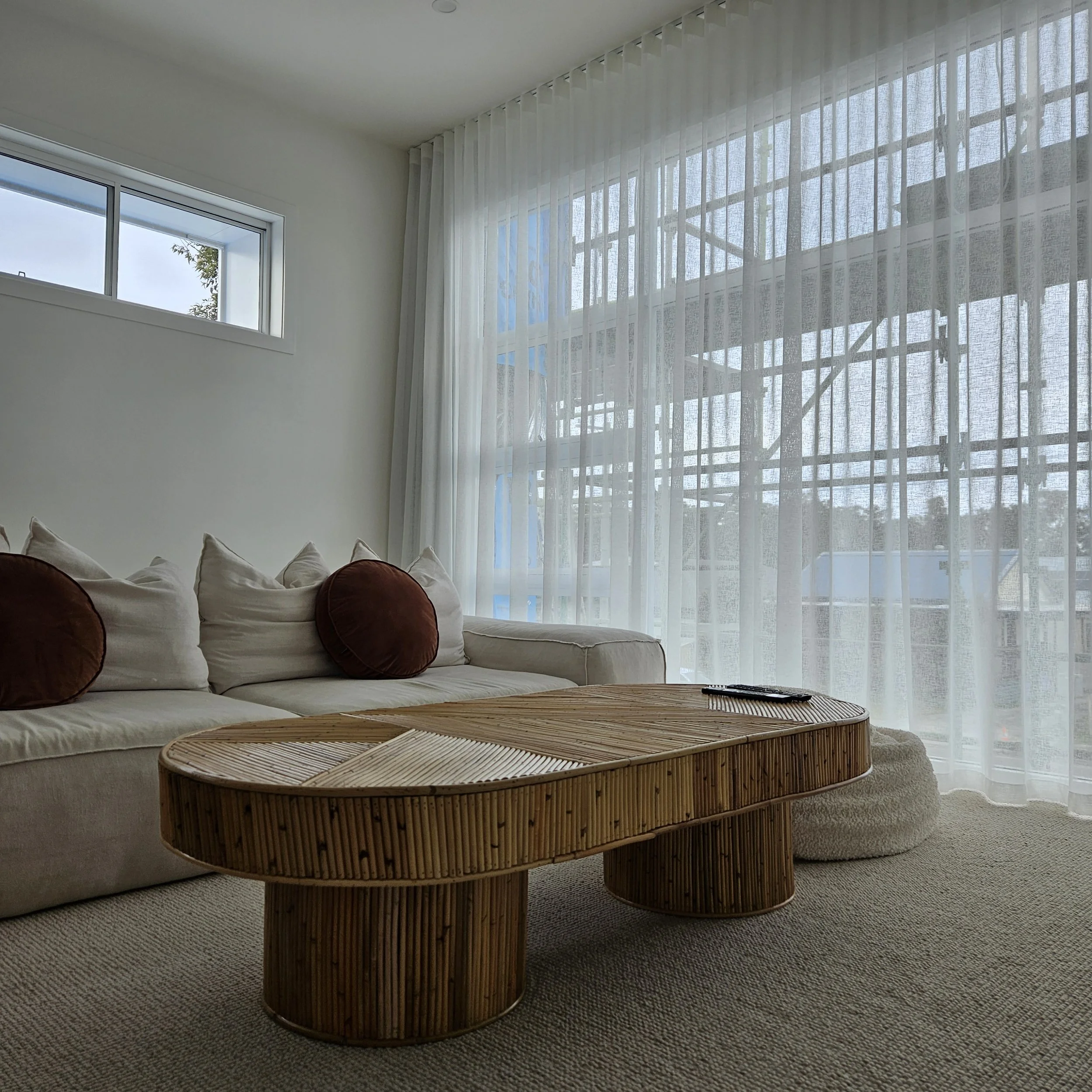 Living room with two couches, a wicker coffee table, sheer curtains, and windows letting in natural light.