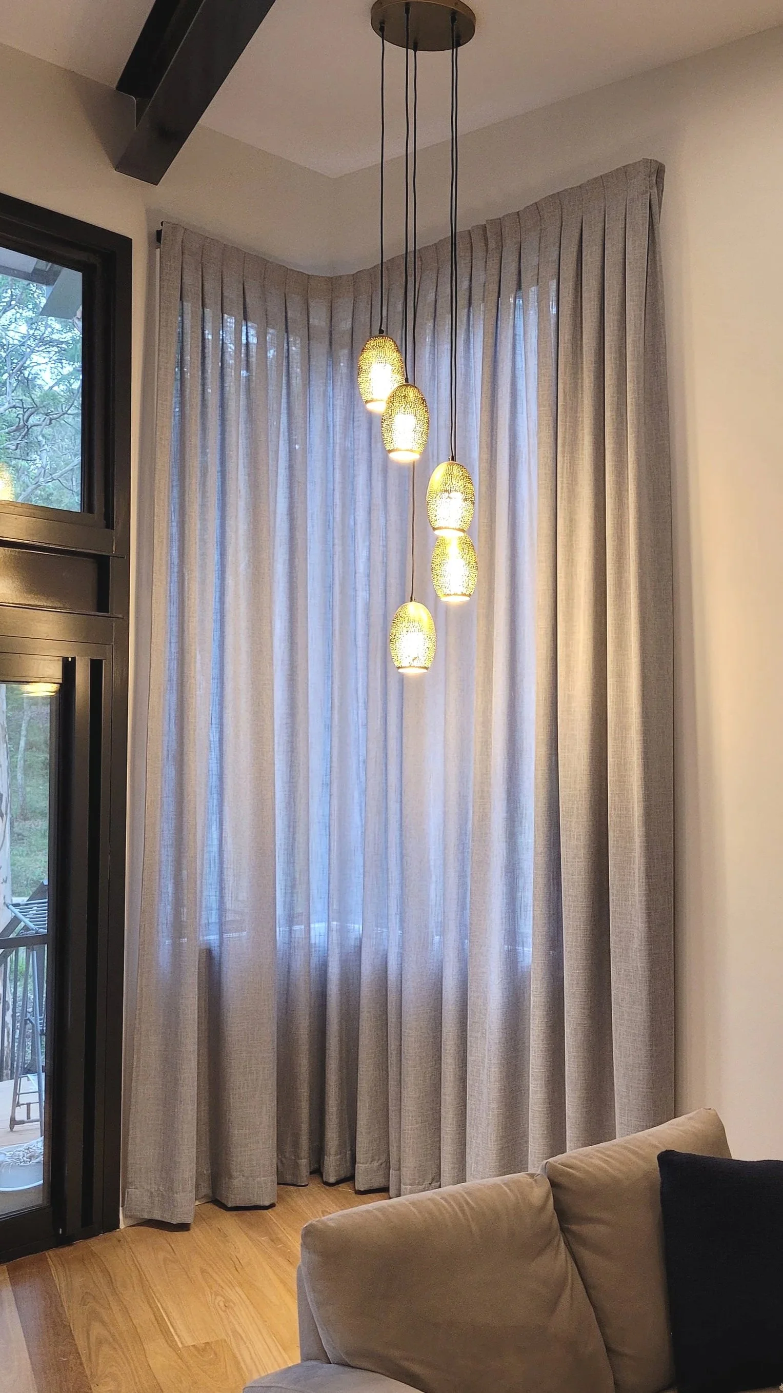 Contemporary living room with beige sofa, large beige curtains, and a modern hanging pendant light fixture with five illuminated oval-shaped lights.