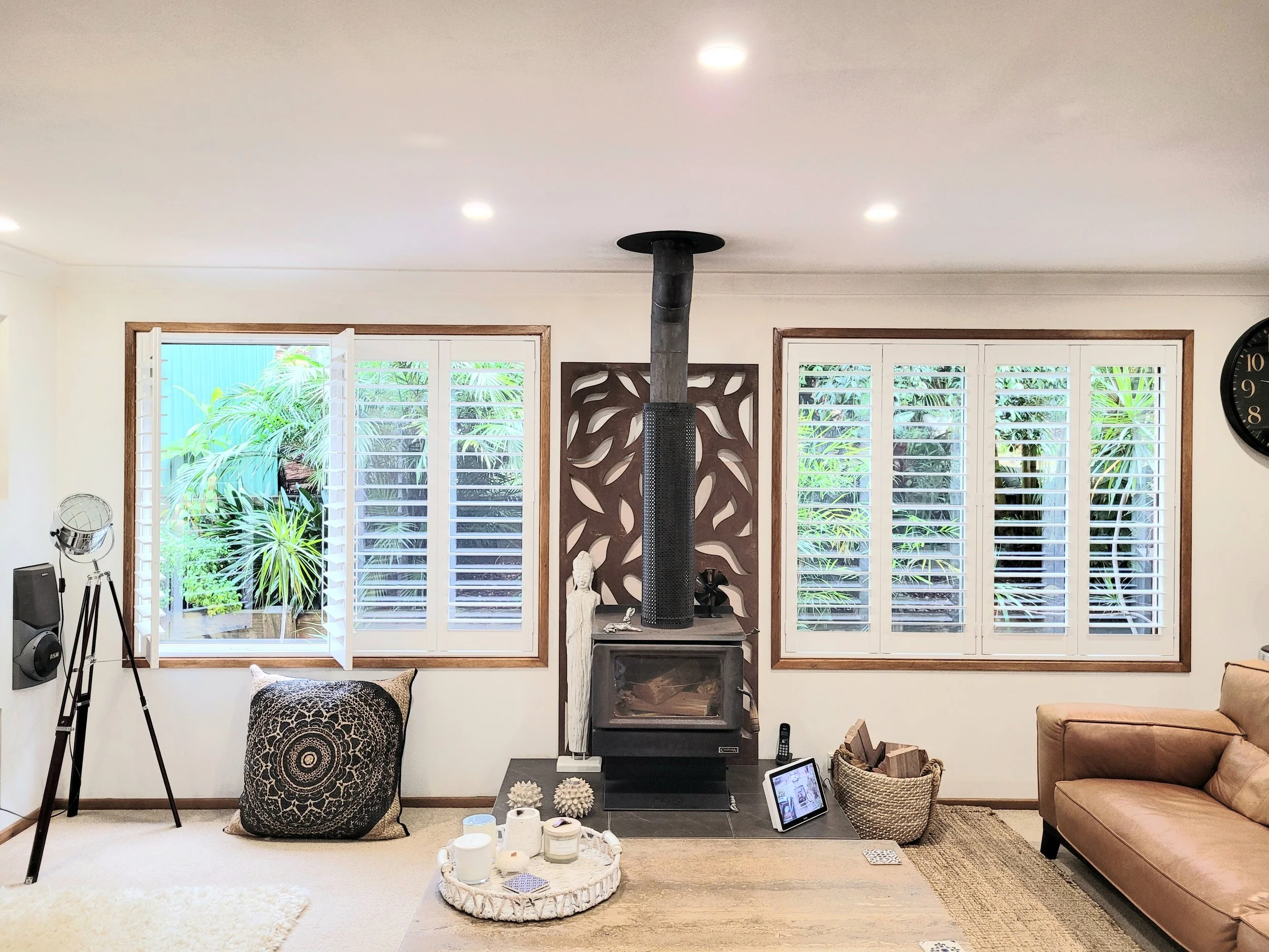 Living room with a wood stove, large windows with shutters, a bean bag, a pillow, various candles on a tray, a tripod lamp, and a sofa.