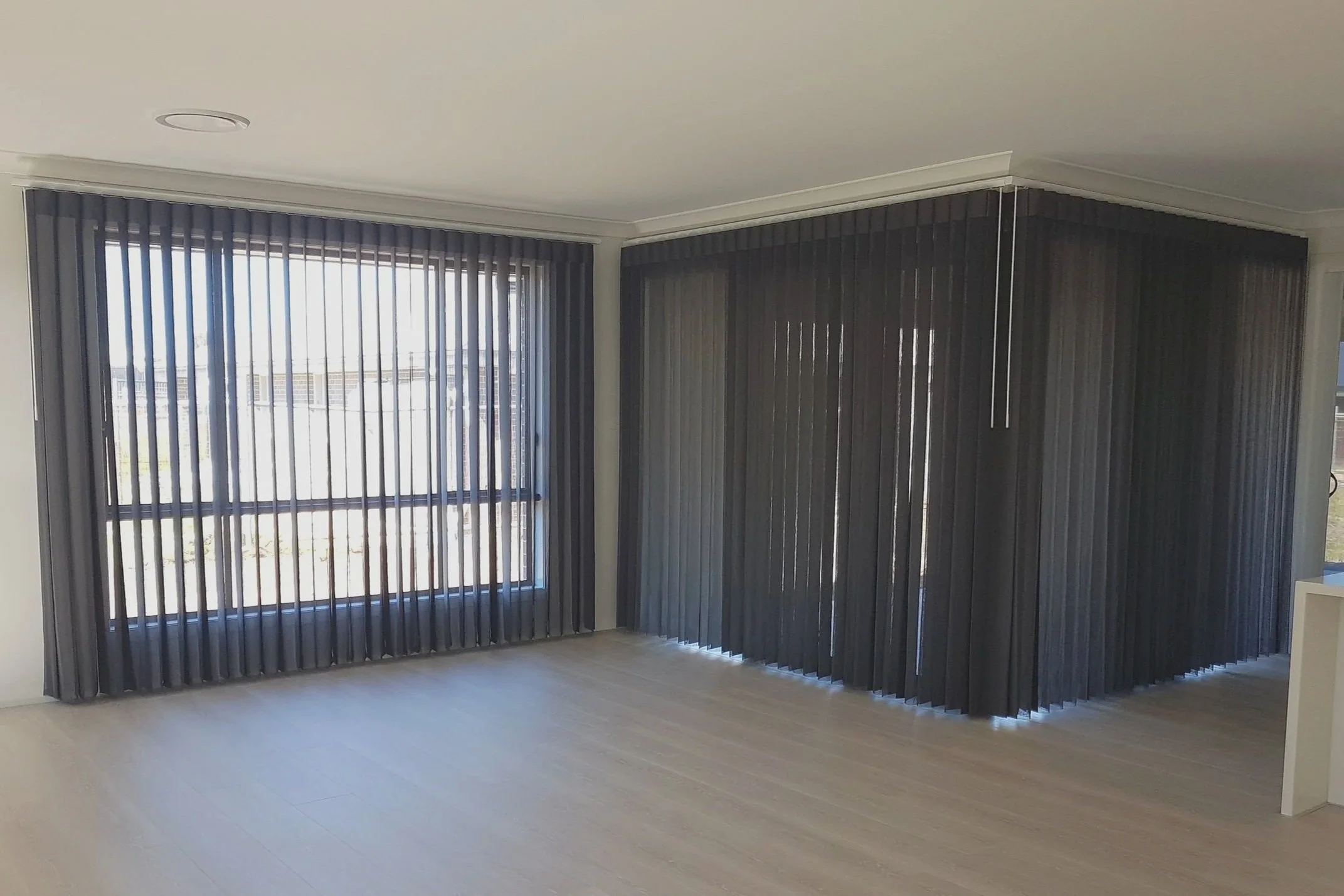Empty room with large windows covered by vertical black blinds.