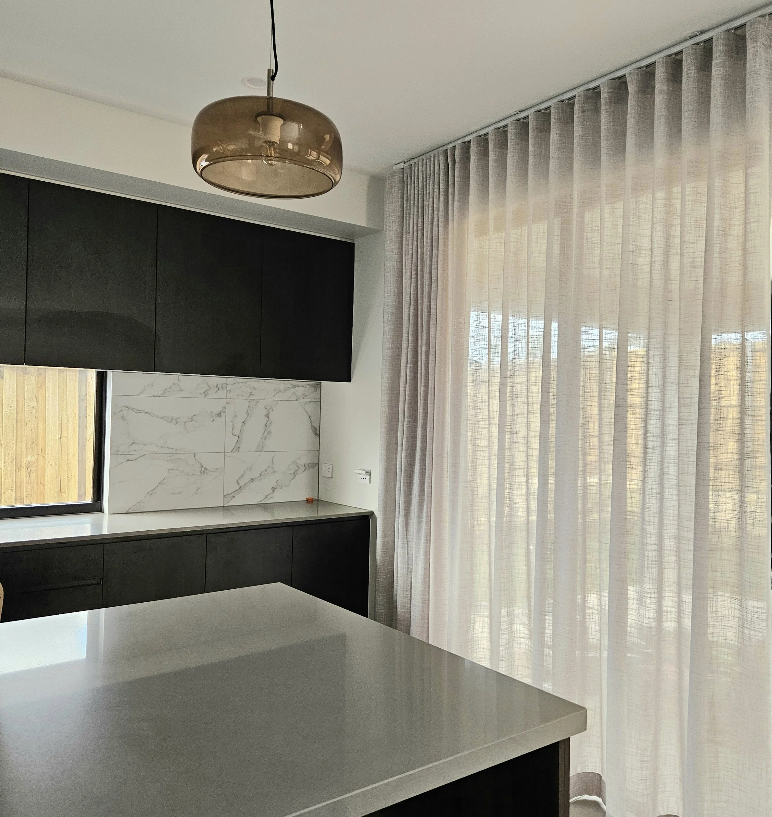 Interior of a modern room with beige curtains, a black cabinet, and a metallic beige ceiling light.