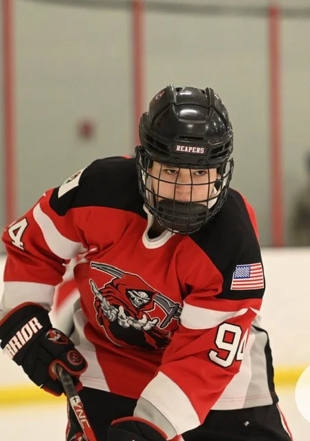 Young hockey player in a red and black jersey on the ice, wearing a helmet and gloves, focused during a game.