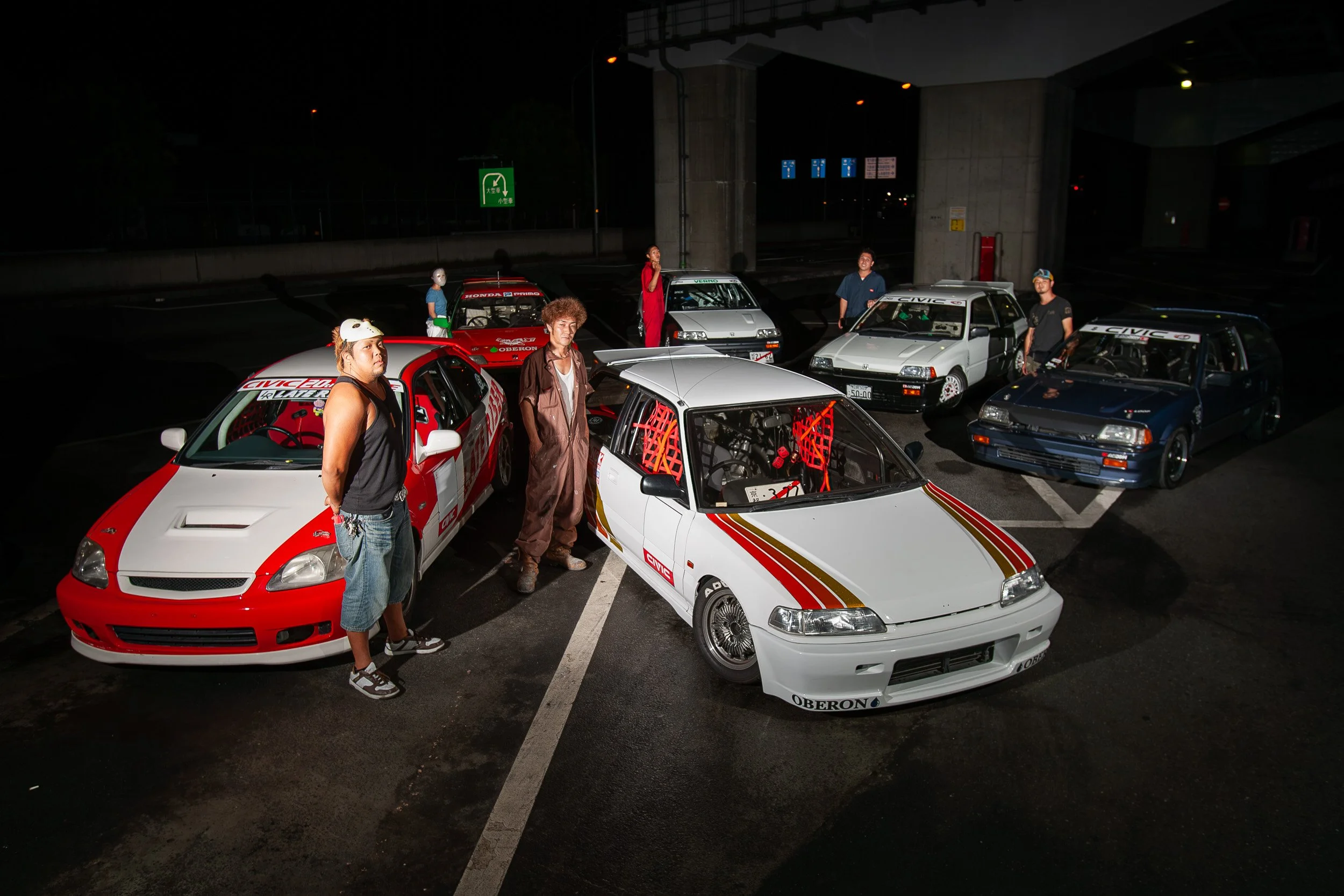 Late Riser Crew members from Osaka's TRA Kyoto posing with their modified Honda Civics at a night meet under a highway overpass.
