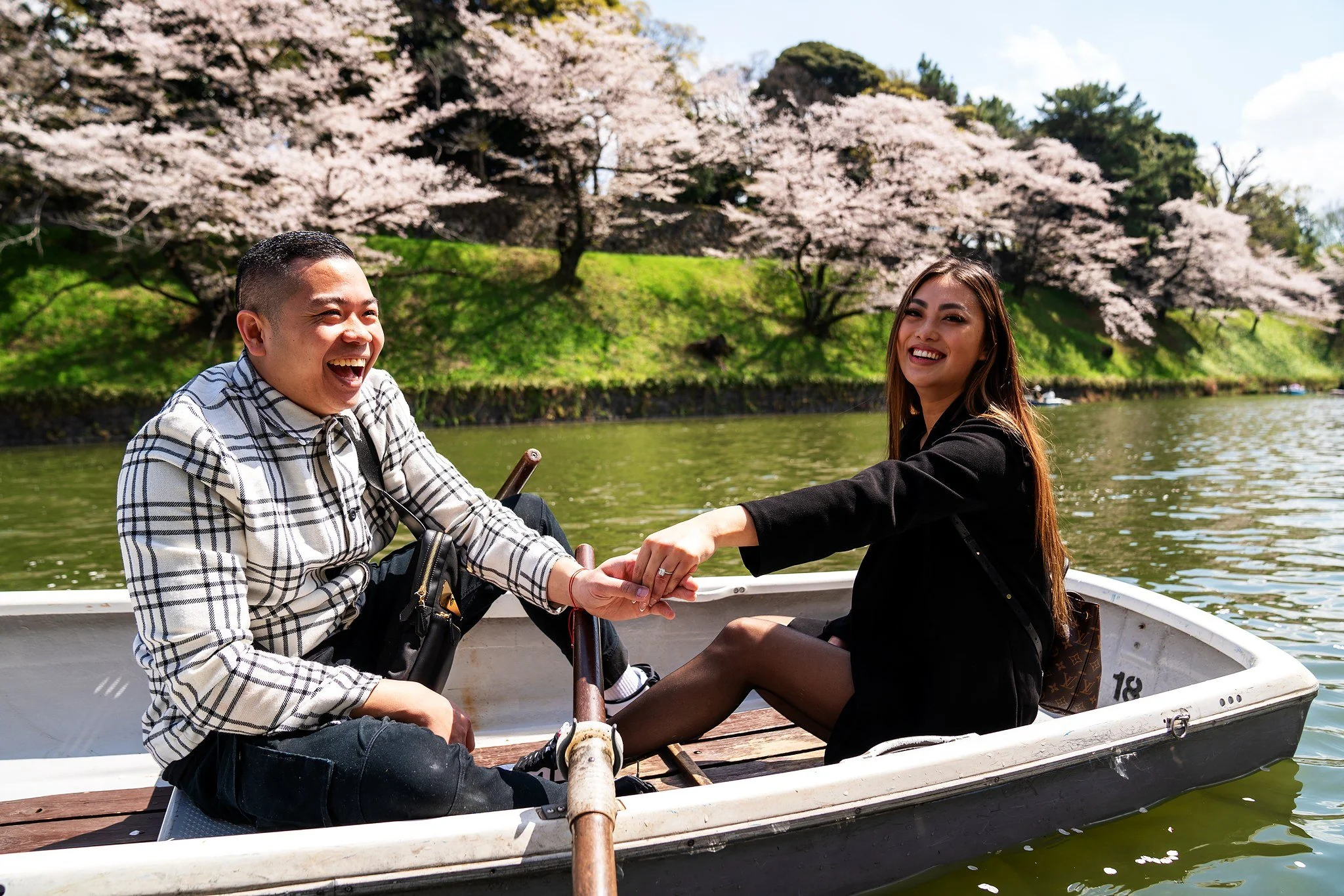 Laughing couple in a rowboat under cherry blossoms at Chidorigafuchi