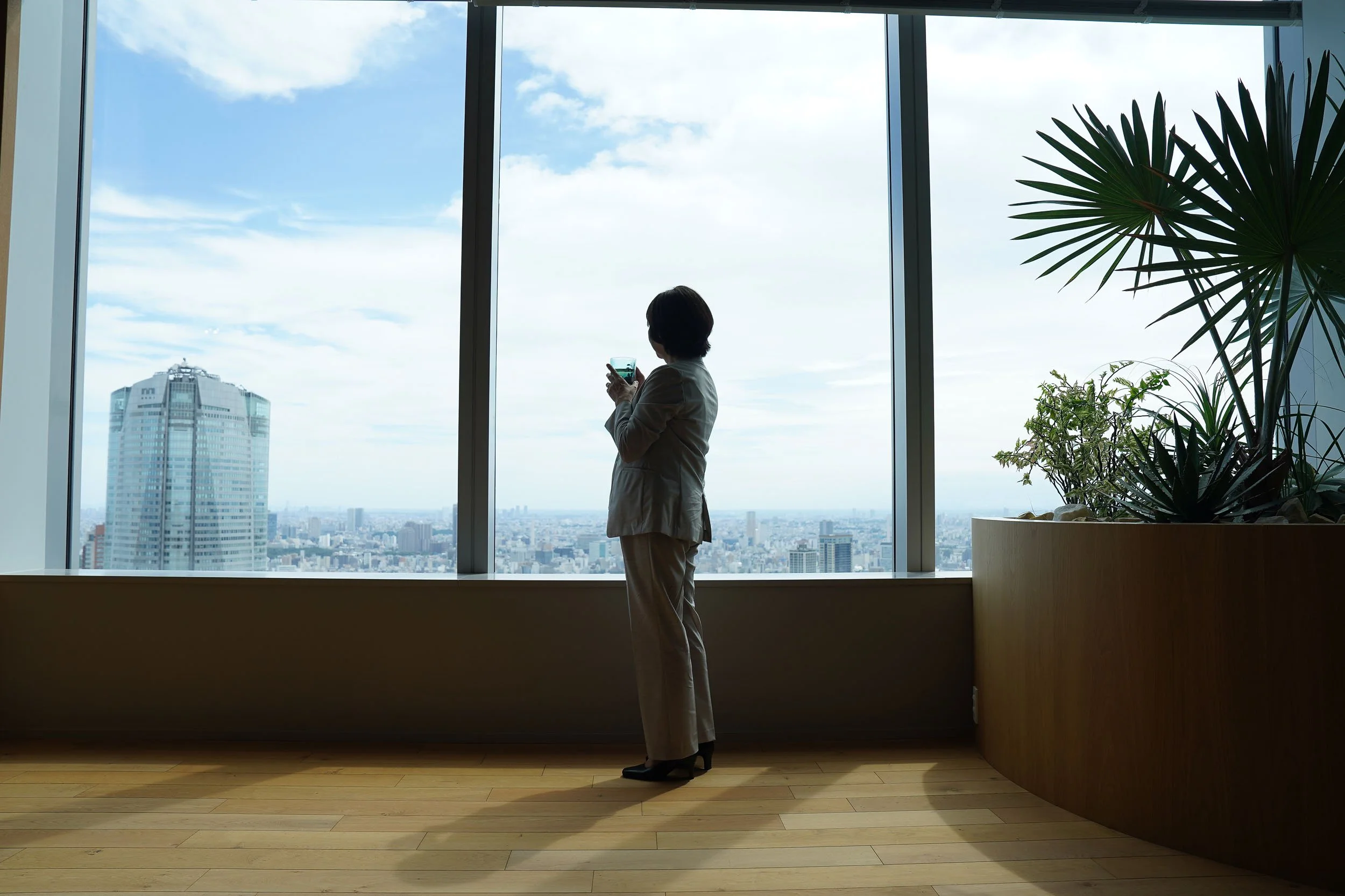 Businesswoman in silhouette gazing out floor-to-ceiling windows at the Tokyo skyline from the Amgen office.