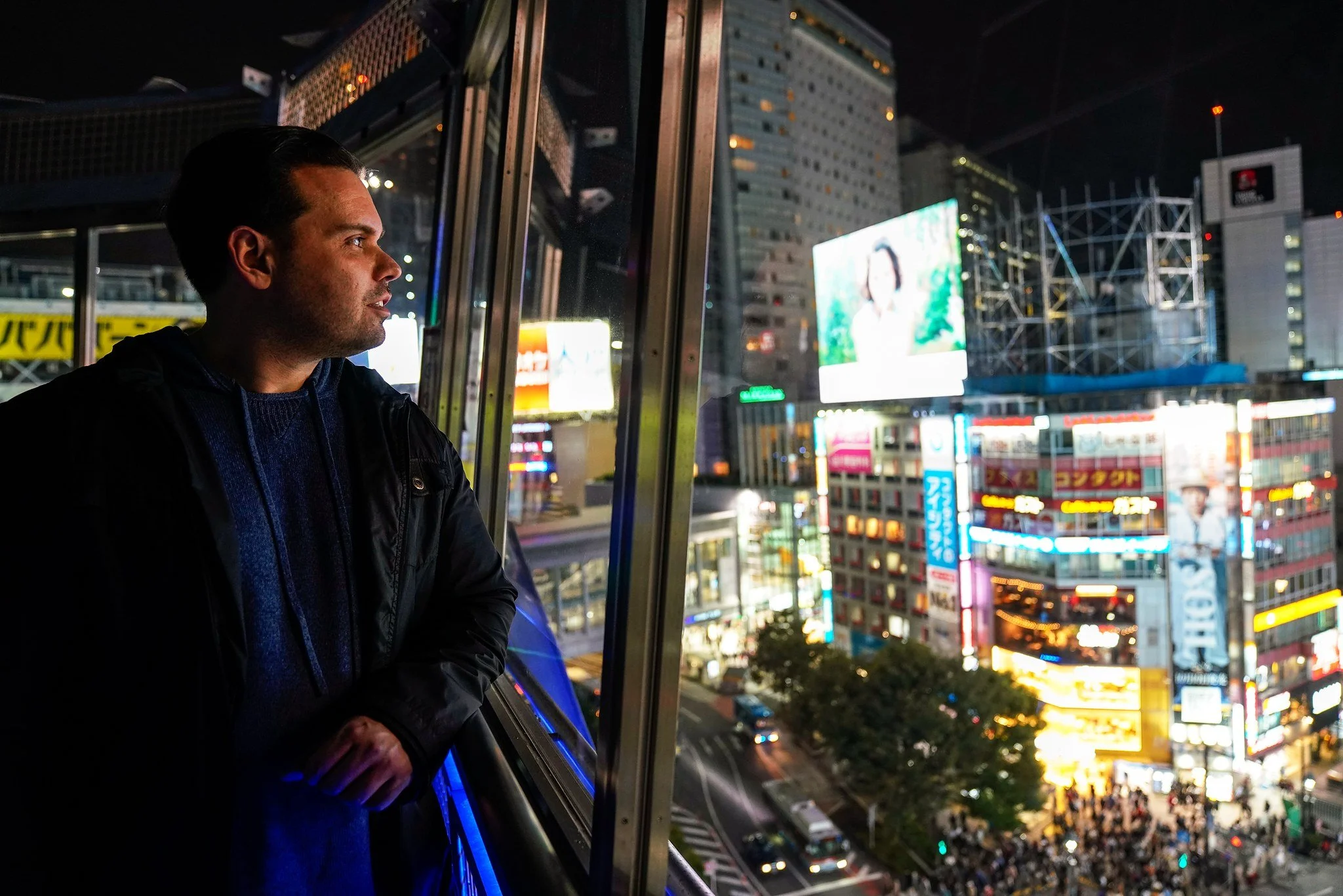 Man looking out over Shibuya Crossing at night from a window above