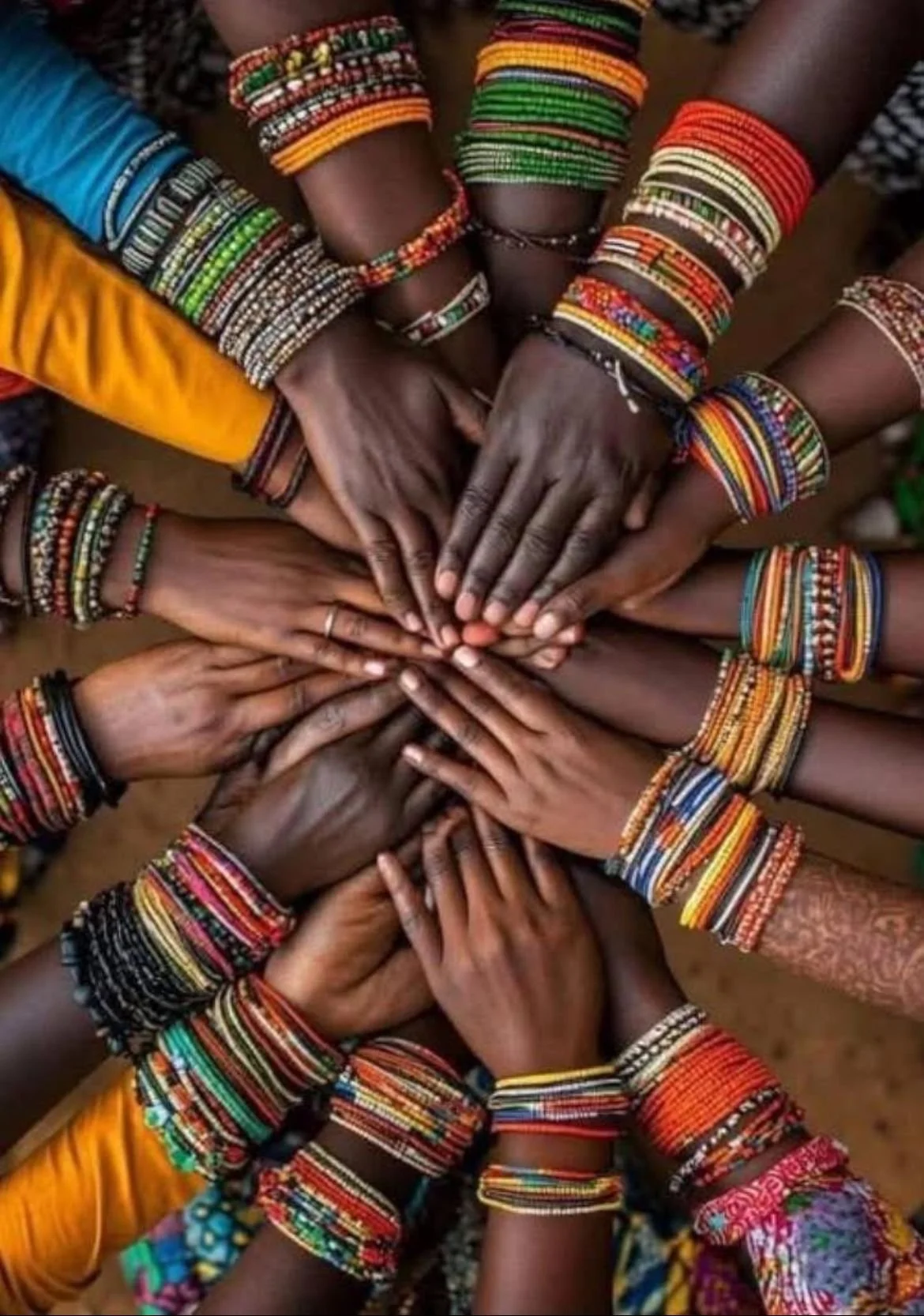 A group of people with dark skin wearing colorful bracelets and clothing, placing their hands together in a circle.