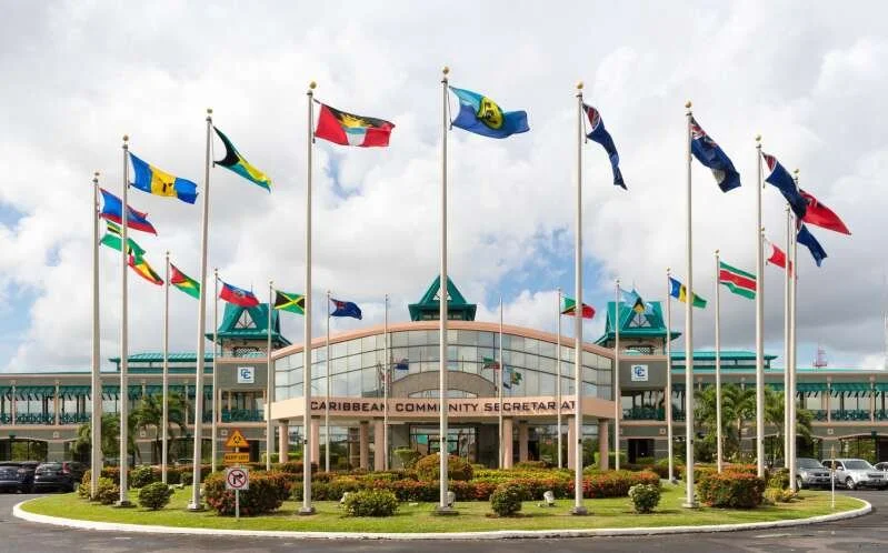 Caribbean Community Secretariat building with flags of different Caribbean nations flying in front.