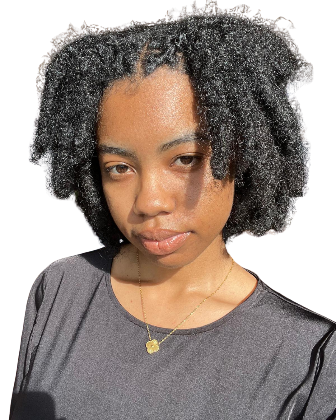 A young woman with natural curly hair, wearing a dark gray shirt and a gold necklace with a four-leaf clover pendant, looking at the camera with a neutral expression.
