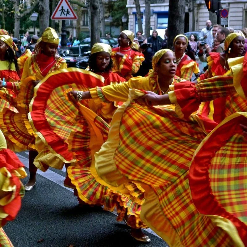 Women dressed in colorful, plaid traditional costumes dancing in a street parade.