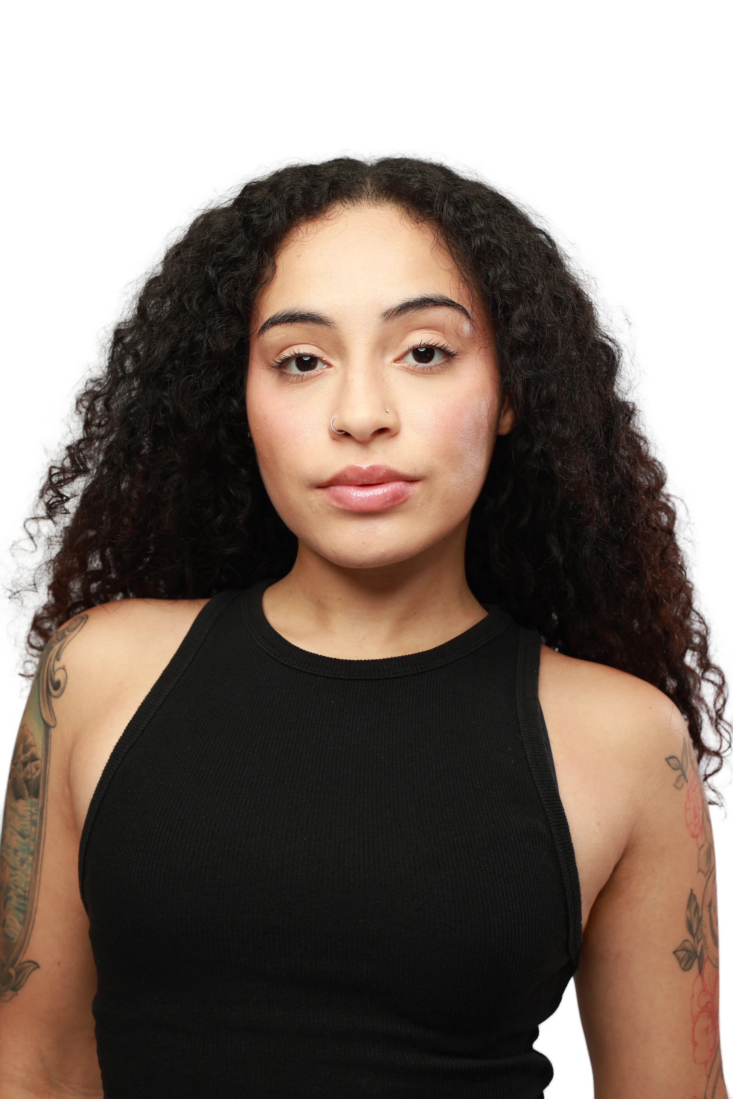 A woman with curly dark hair wearing a black sleeveless top, looking directly at the camera with a neutral expression.