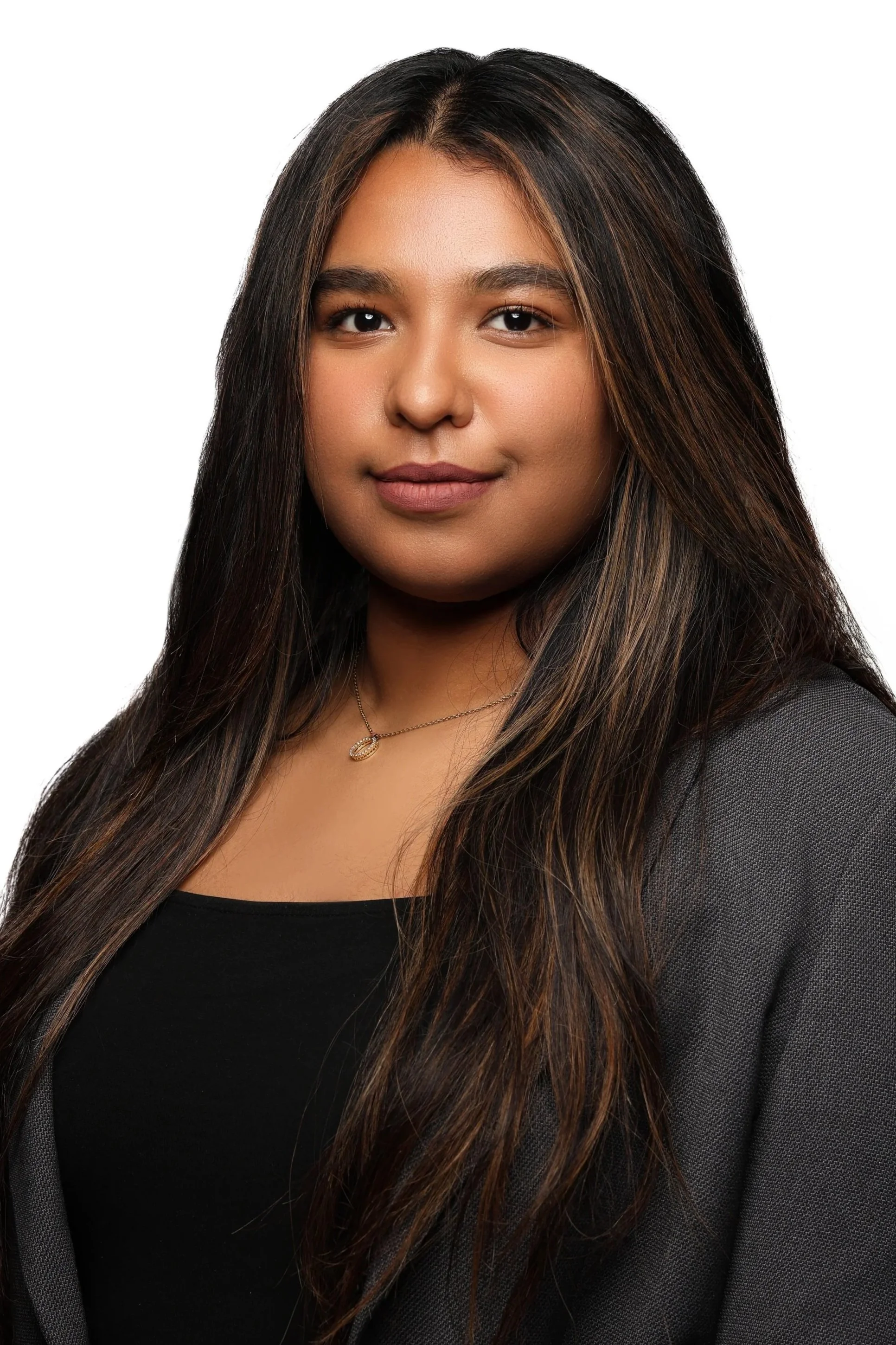 A woman with long dark hair and light brown skin, wearing a dark top and blazer, smiling softly, with a white background.