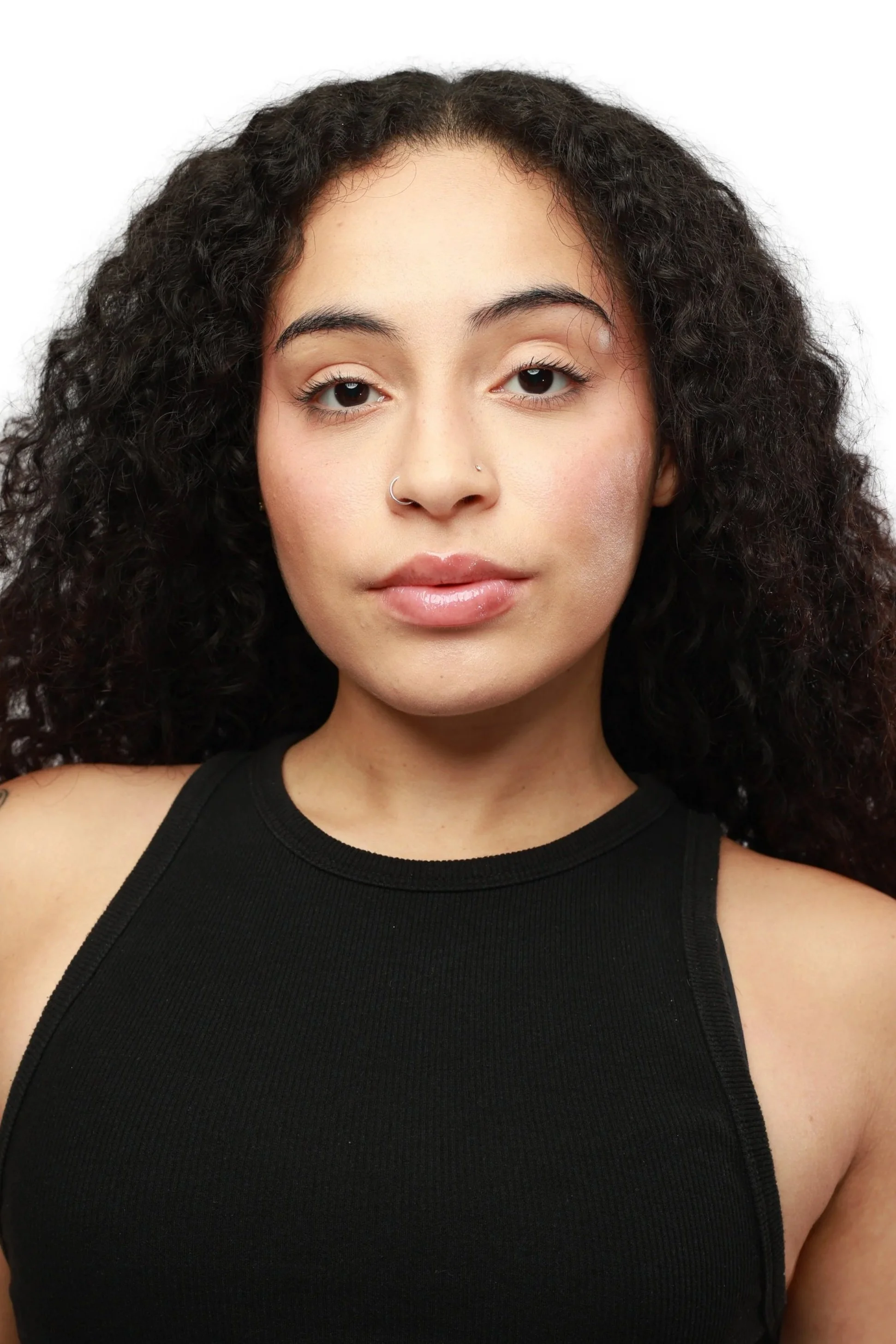 A woman with curly dark hair wearing a black sleeveless top, looking directly at the camera against a plain white background.