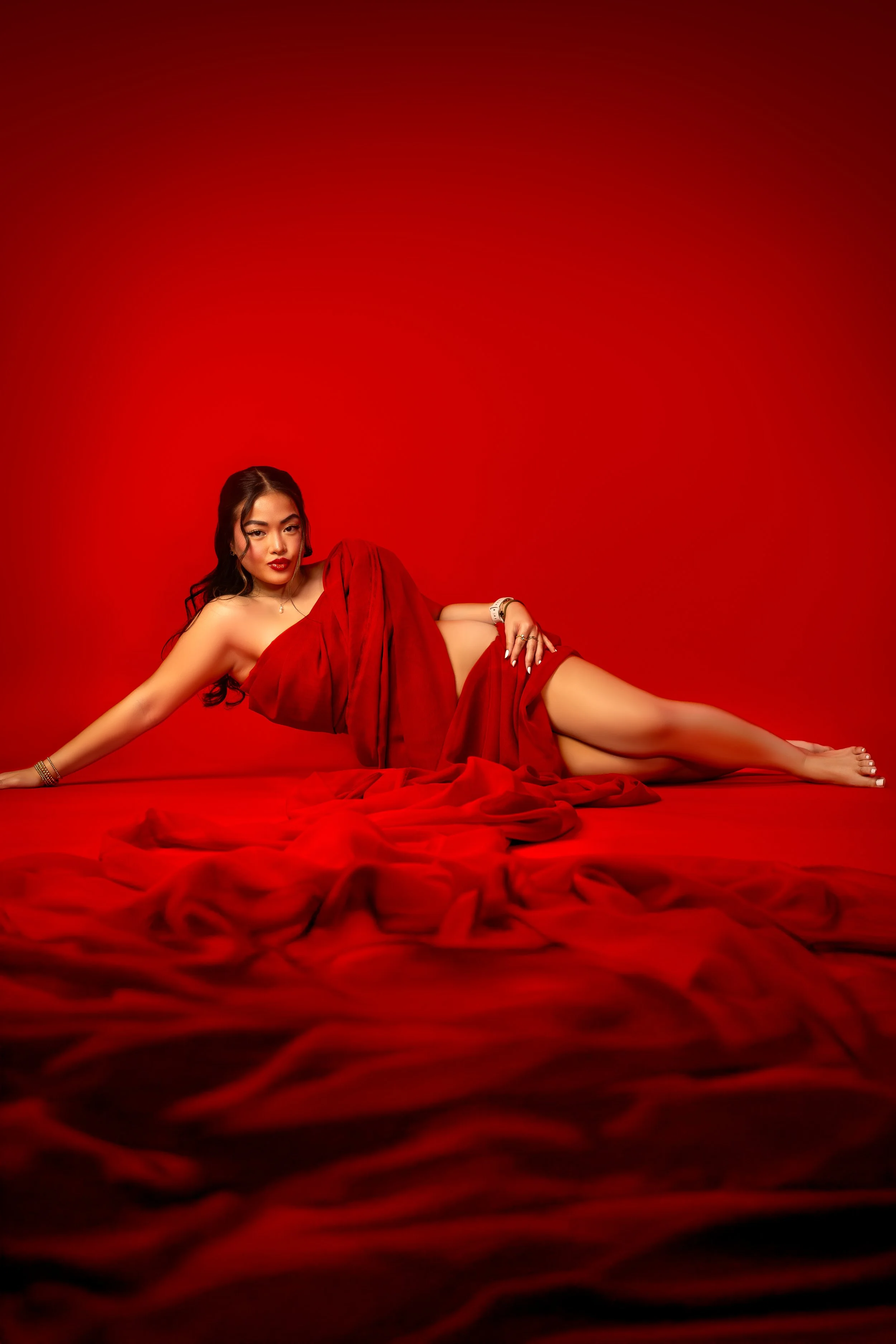 Woman in red dress lying on red fabric with red background, looking at camera.