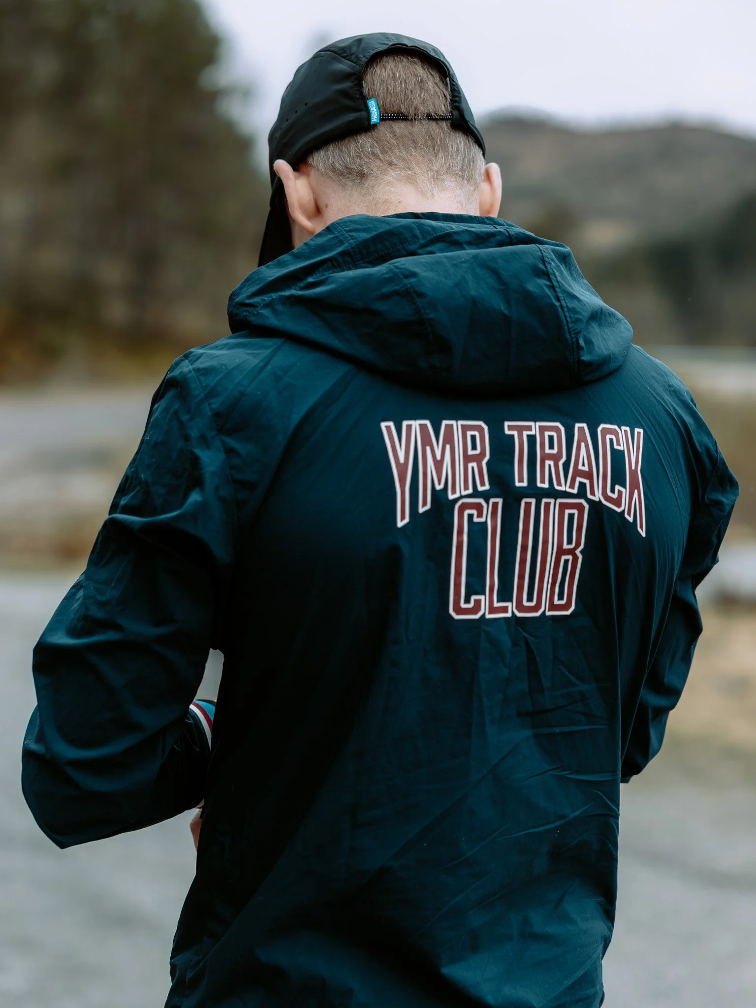 Ein person som joggar utandørs, sett bakfrå, iført svart jakke med teksten «YMR Track Club».