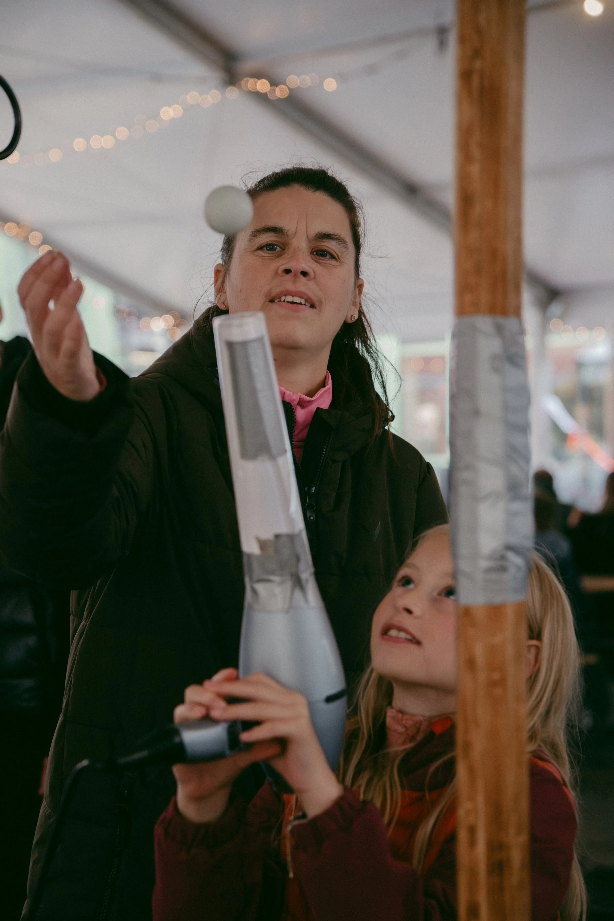 Ei kvinne og eit barn som blæs opp ein ballong saman innandørs, med julelys i bakgrunnen.