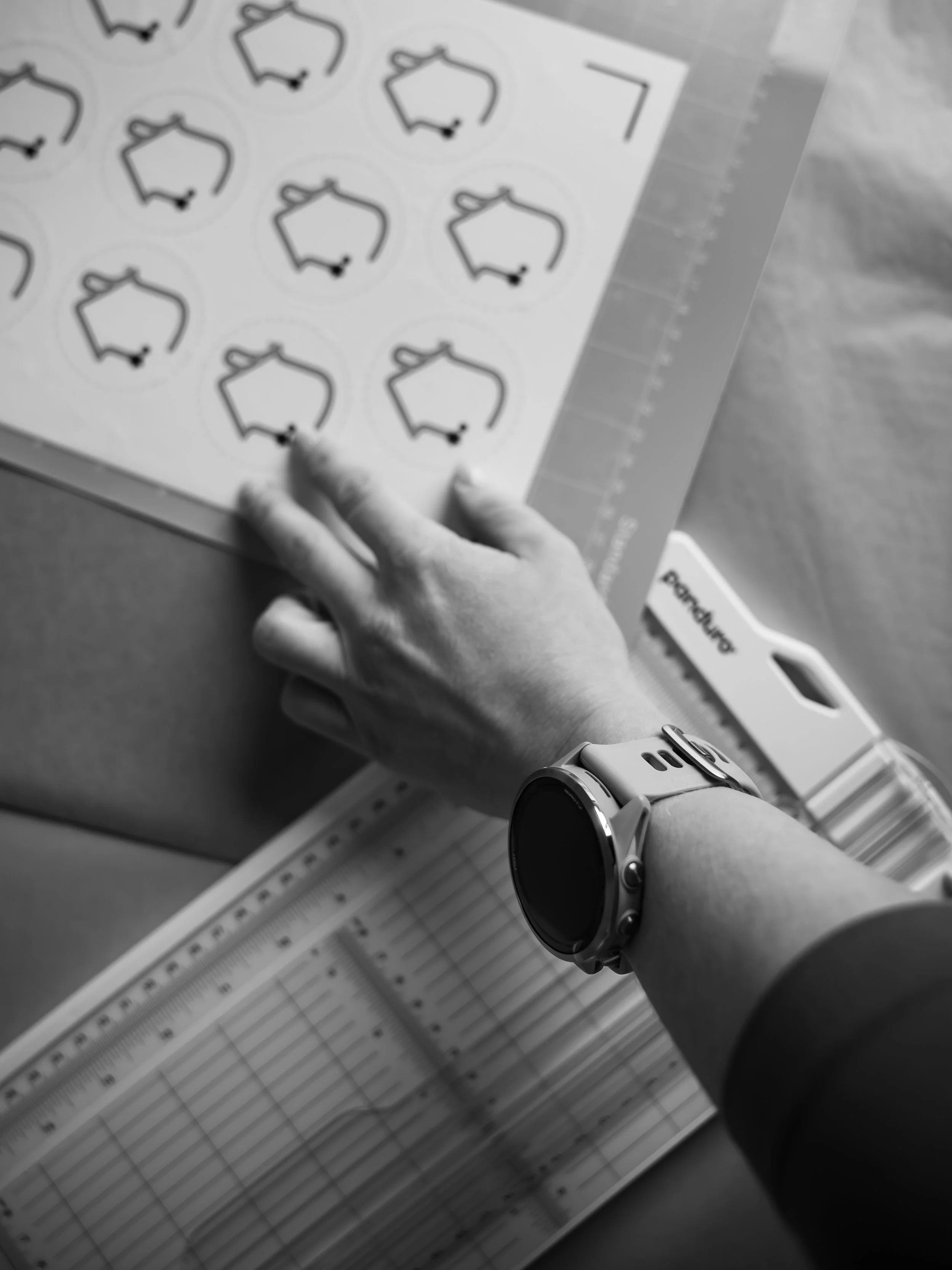 Ein person som måler avstand eller lengde, med svart klokke og kvit langarma skjorte. I bakgrunnen er ei måleplate med centimeter- og tommeinndeling.